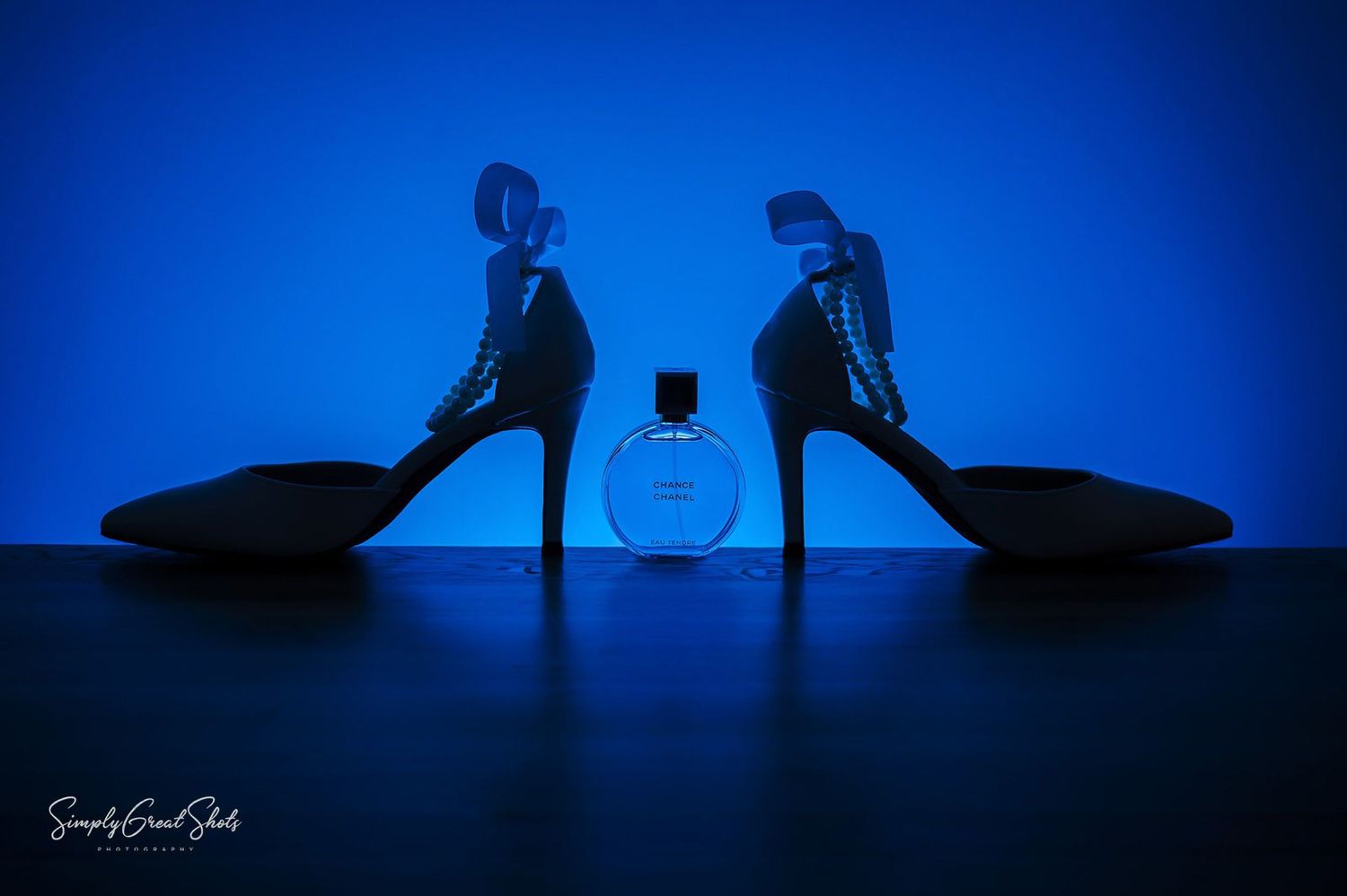 A silhouette photograph of brides shoes and perfume backlight by a blue light.