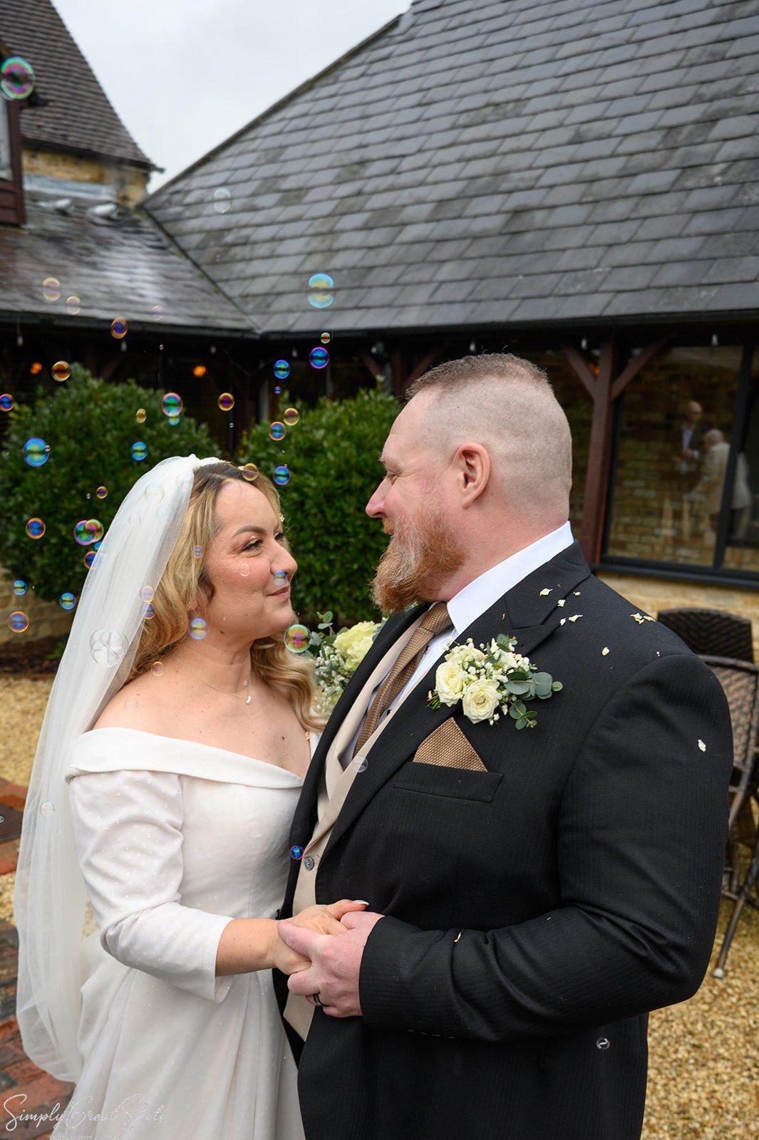 Newlyweds celebrating outside voco Oxford Thames manor house with confetti bubbles and stone architecture backdrop