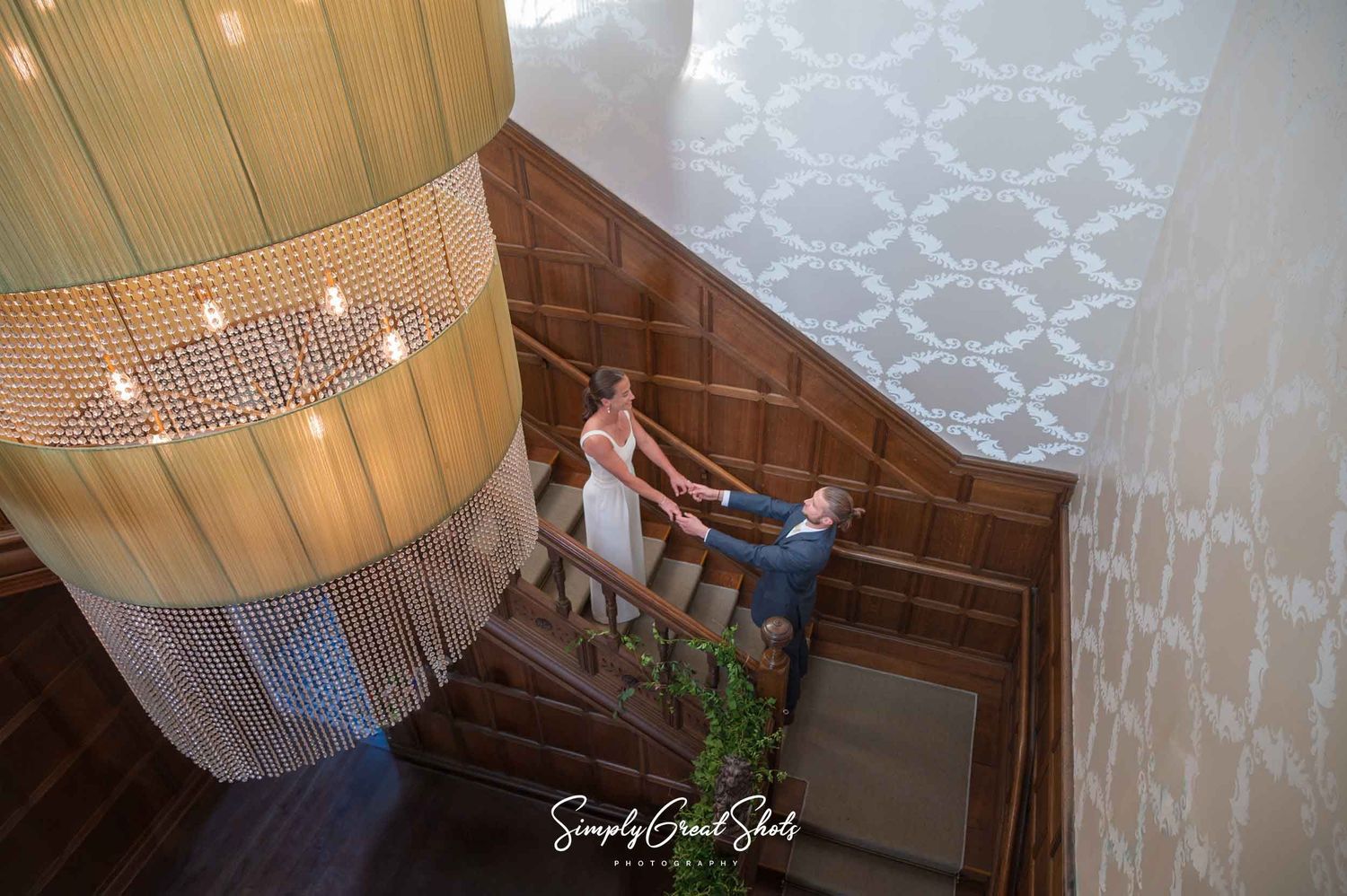 Hampton Manor wedding photographer captures a wedding couple portrait on a grand spiral staircase with a huge chandelier.