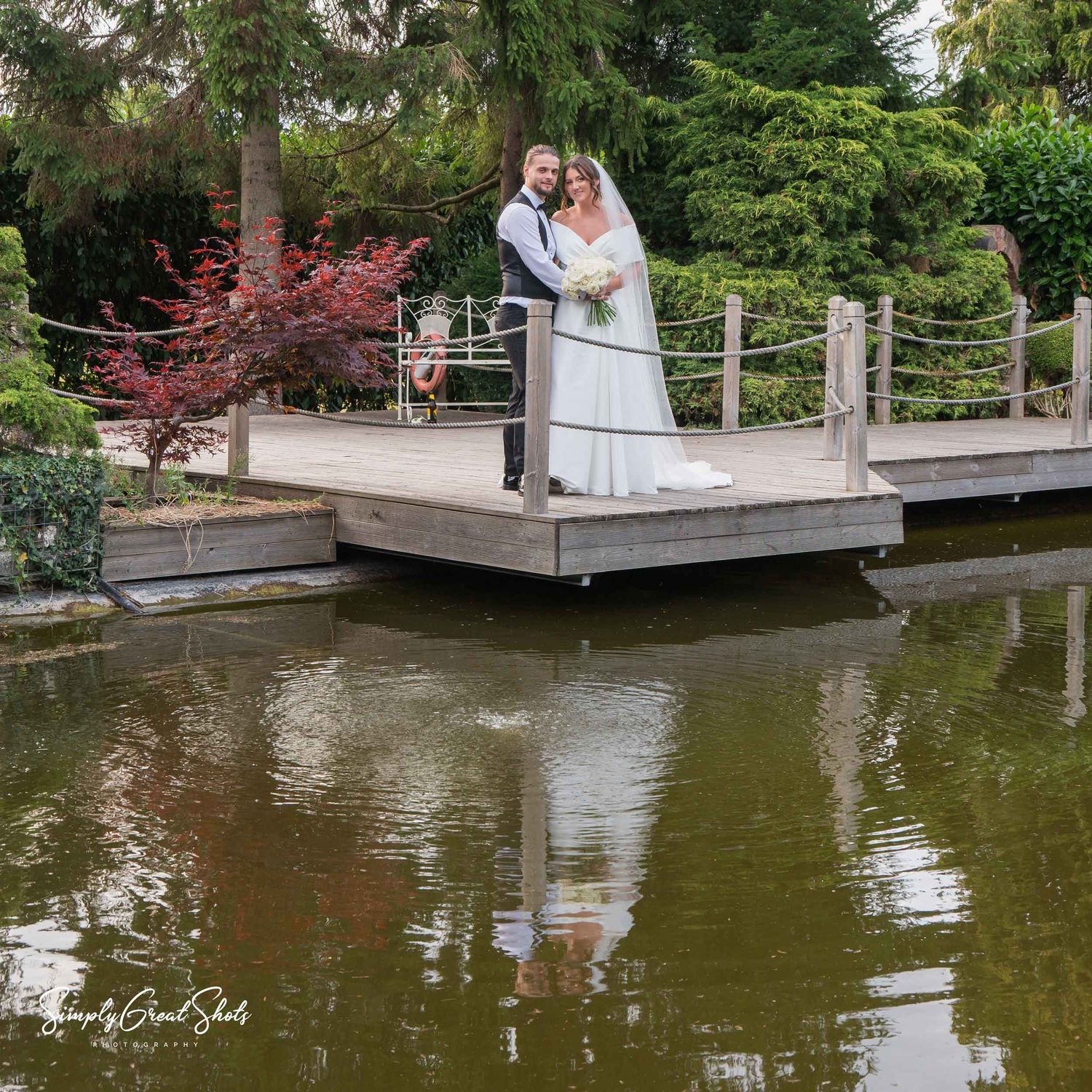 Redhouse Barn wedding photographer captures the newlyweds posing on decking overlooking the koi pond.