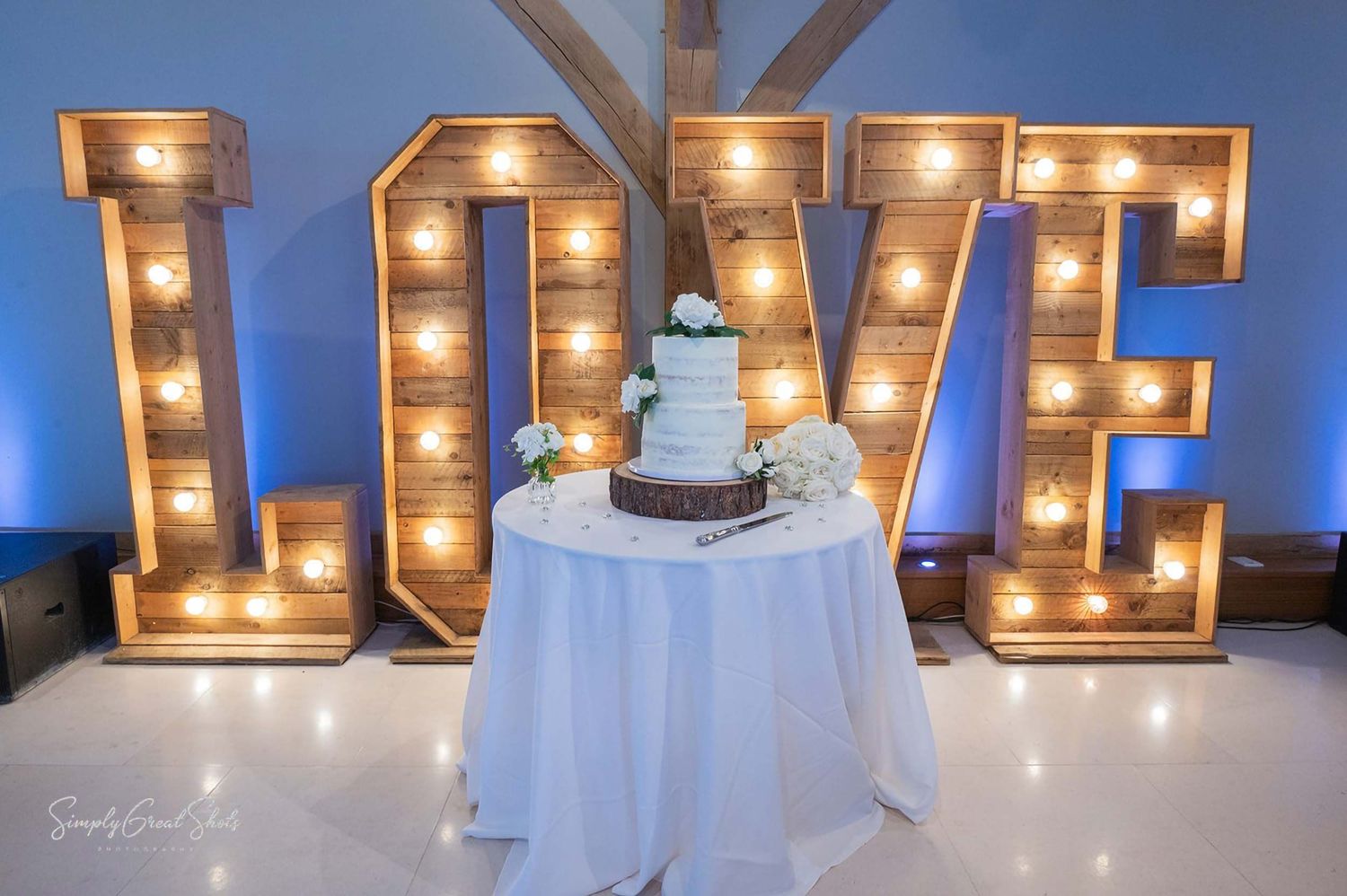 A two-tiered wedding cake on display in front of an illuminated love sign at a Coventry wedding venue