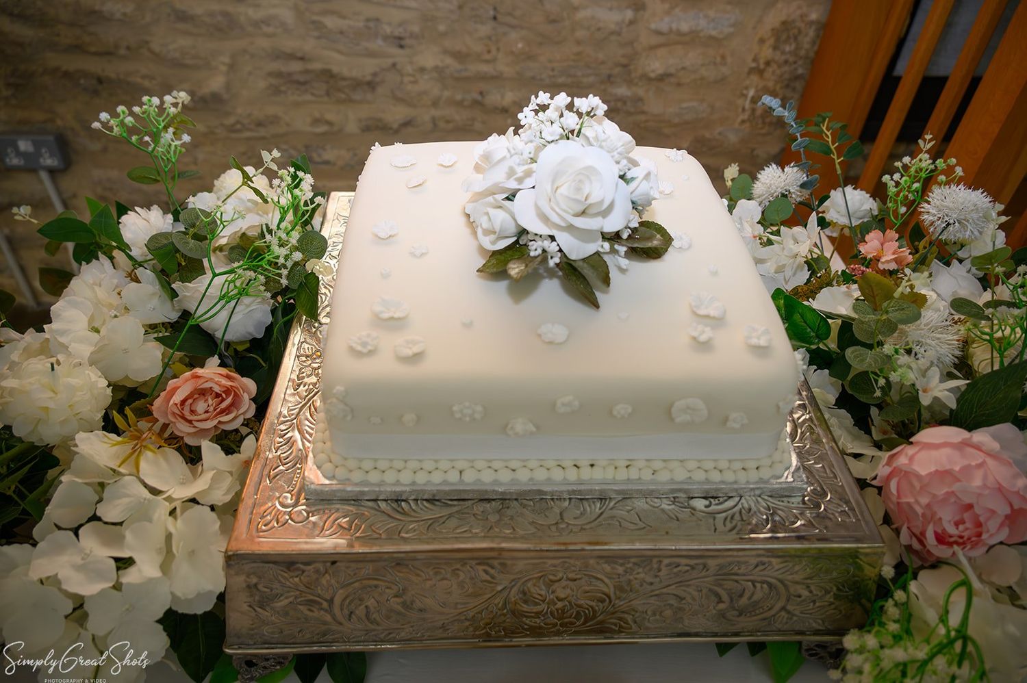 Classic white square wedding cake decorated with sugar roses and fresh flowers on ornate silver stand
