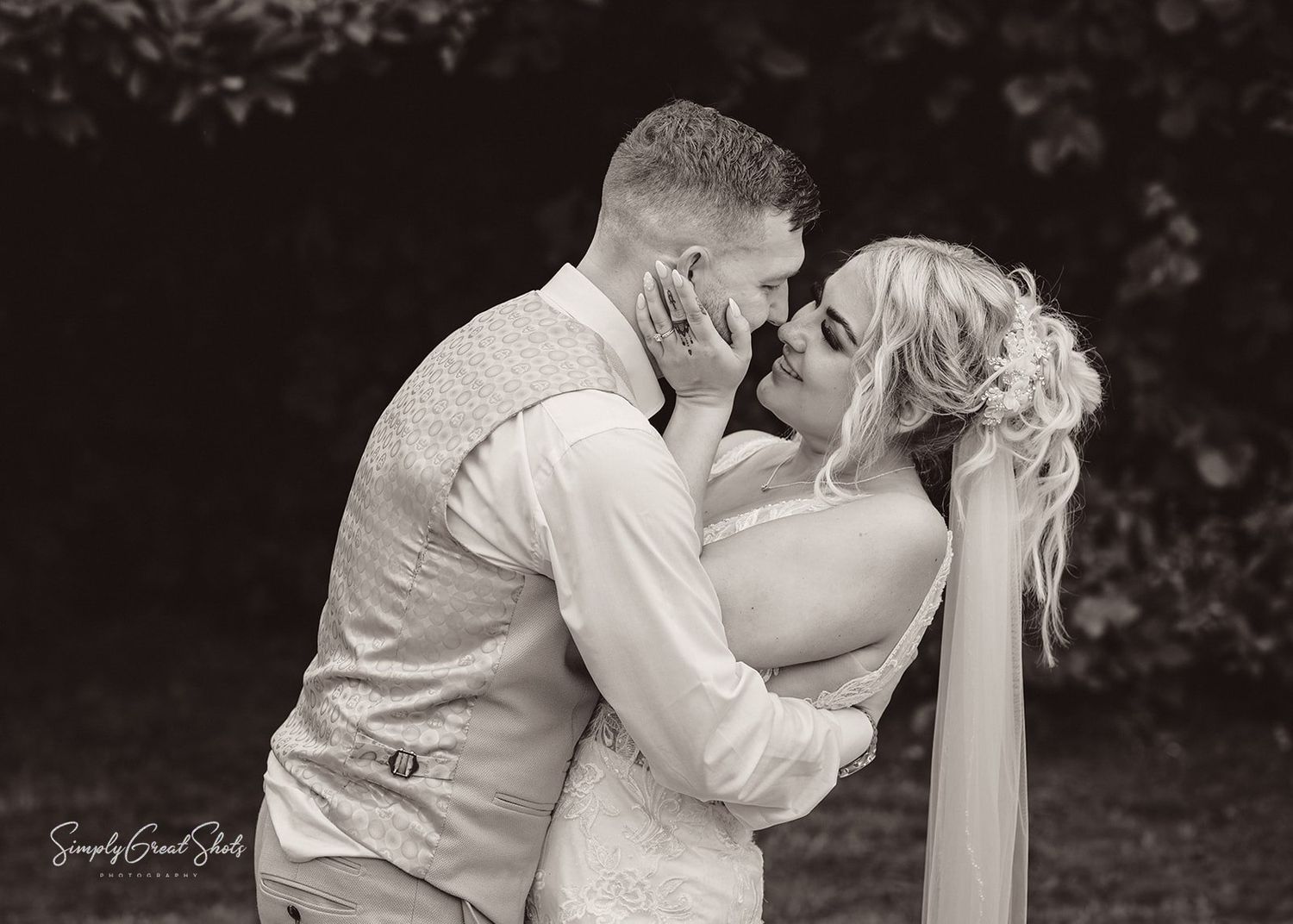 Black and white photograph showing a wedding couple in romantic embrace during an outdoor photoshoot.