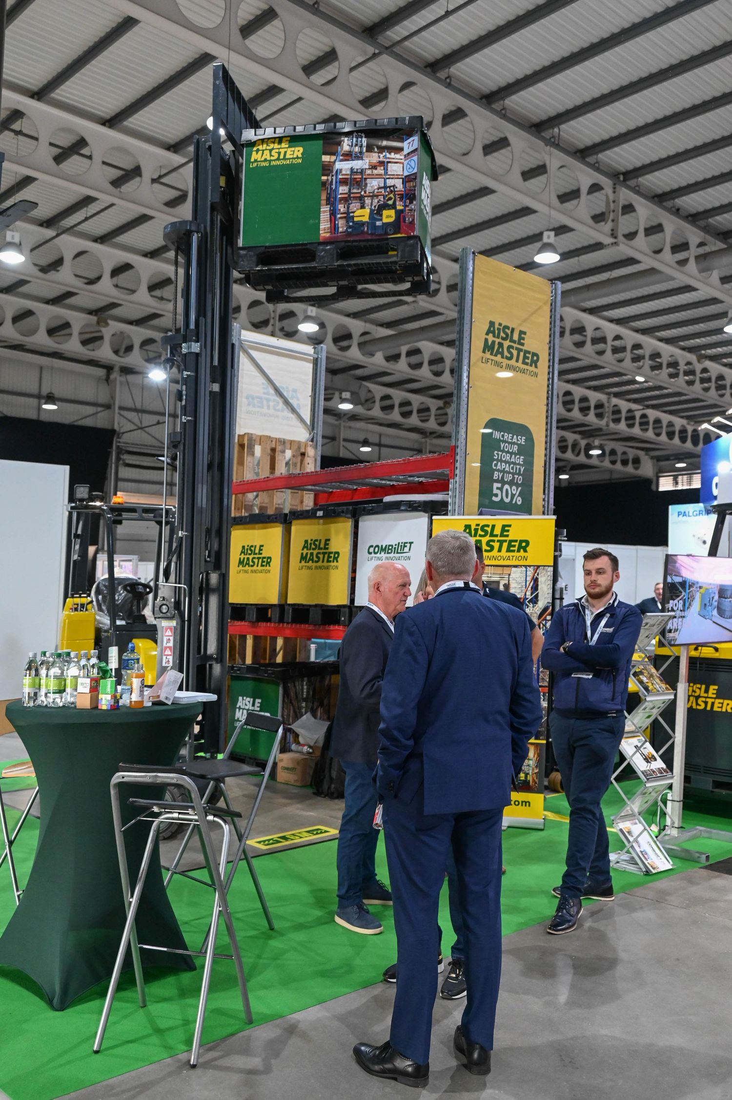Trade show booth display with green carpet and products on shelves, visitors examining agricultural equipment at convention.