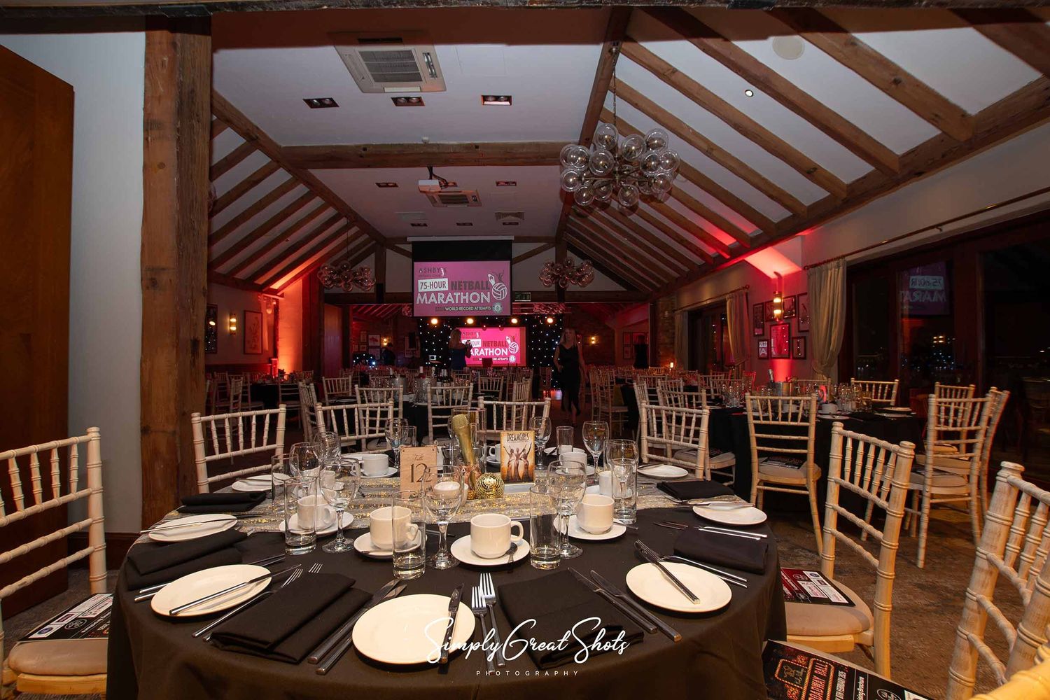 A formal dining setup with black tablecloths, chiavari chairs, and red accent lighting in an elegant reception venue.