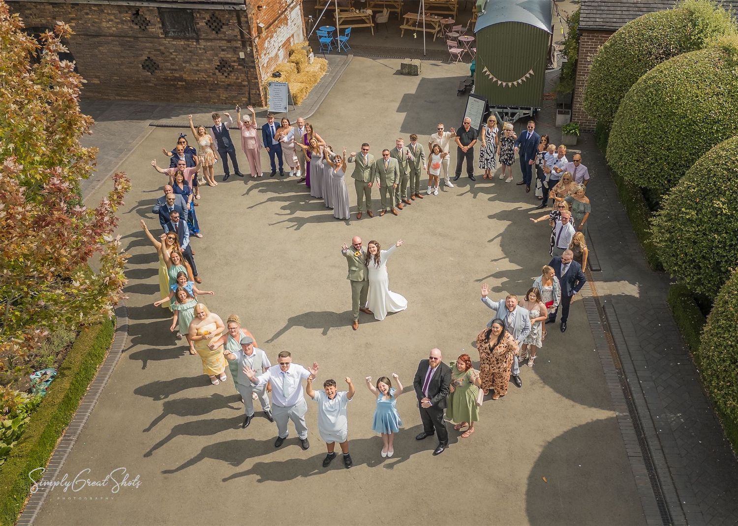 The wedding guests surround the bride and groom, creating a heart shape which was captured by SimplyGreatShots Photography