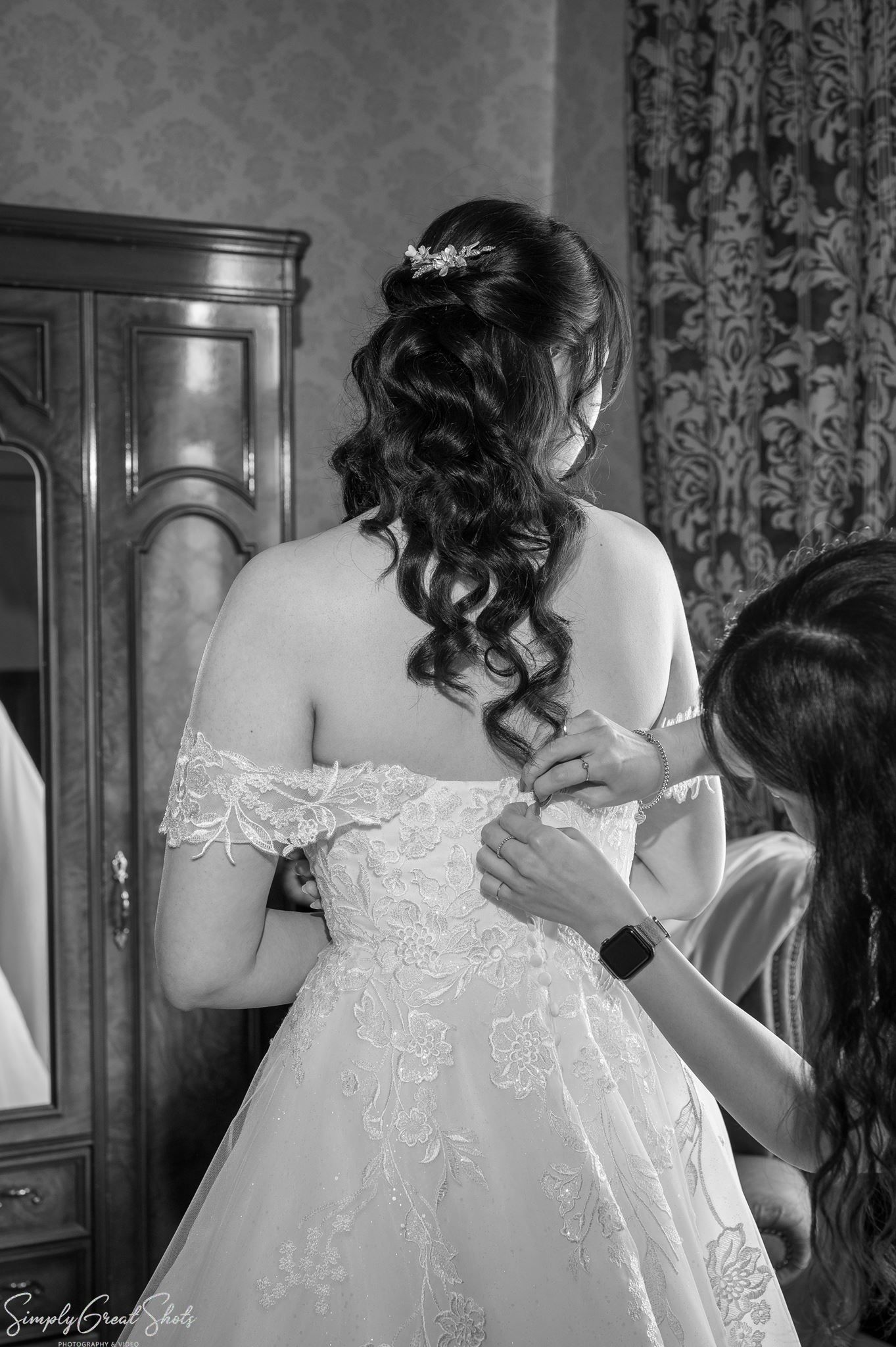 Bride Minky being helped into her white off-the-shoulder wedding dress at Coombe Abbey Warwickshire.