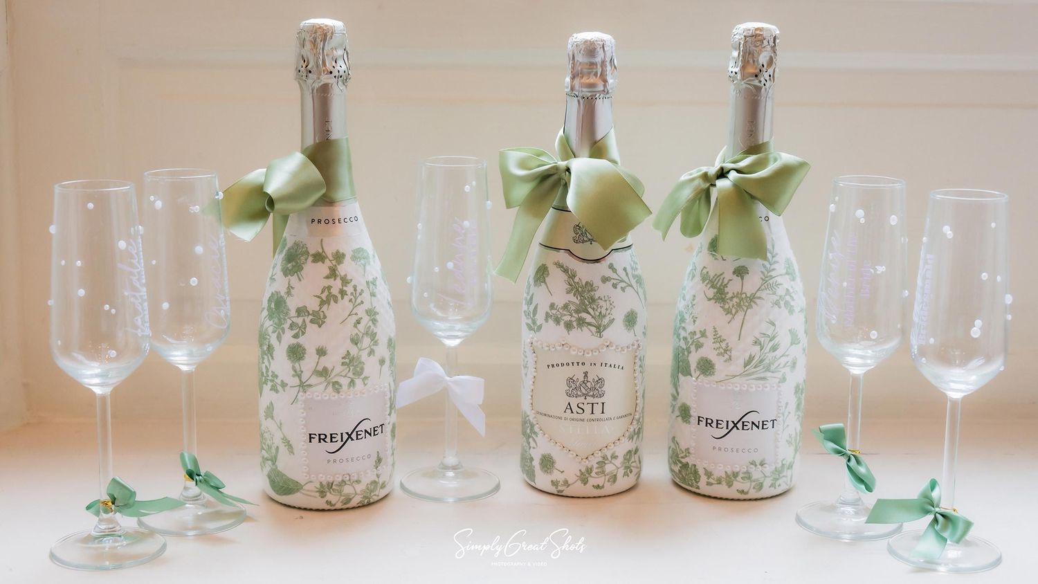 Three bottles of Freixenet sparkling wine with sage green bows and a champagne glass at Rothley Court wedding.