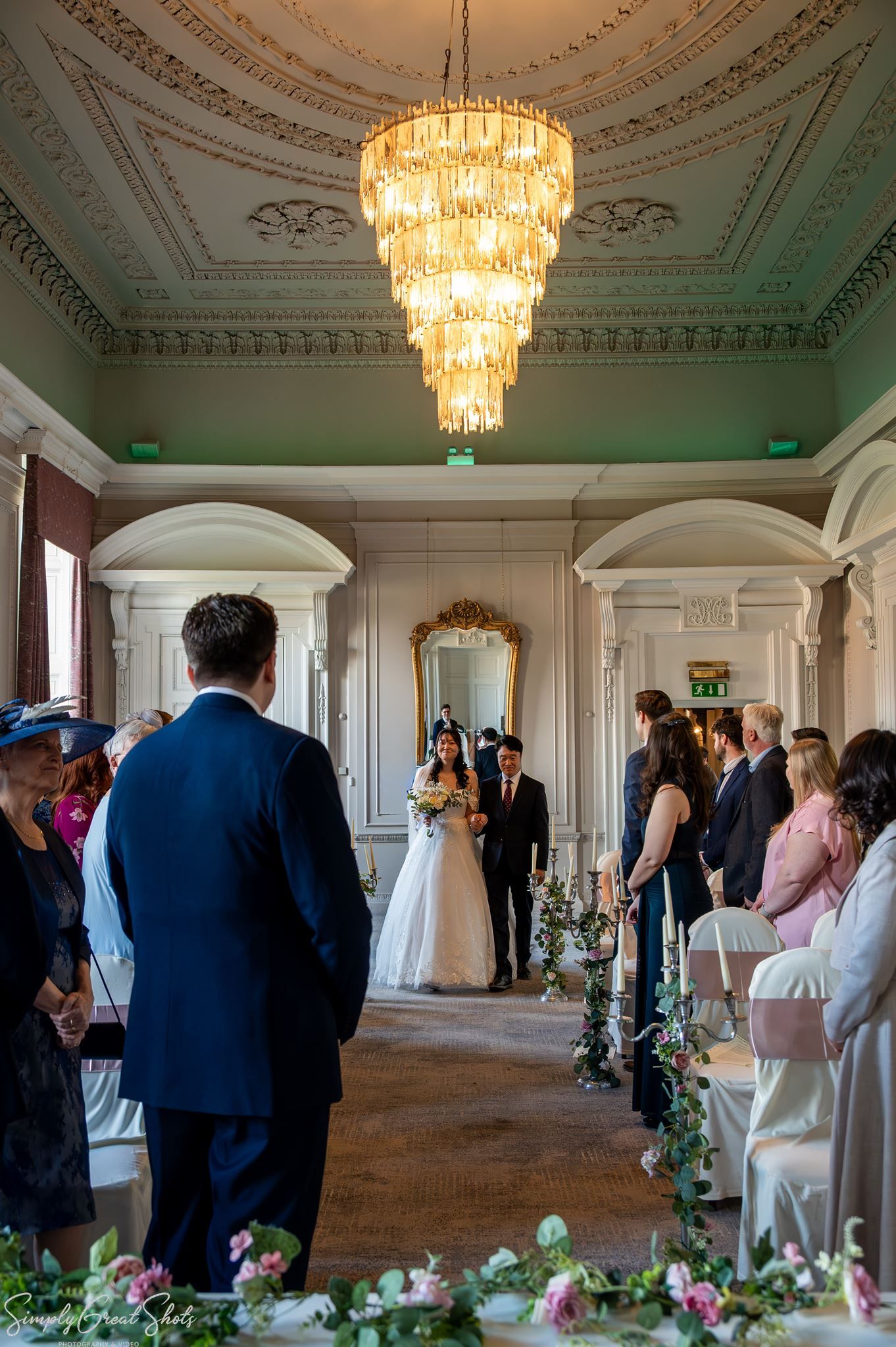 Bride Minky walking down the aisle in The Cloisters at Coombe Abbey towards groom Mark.