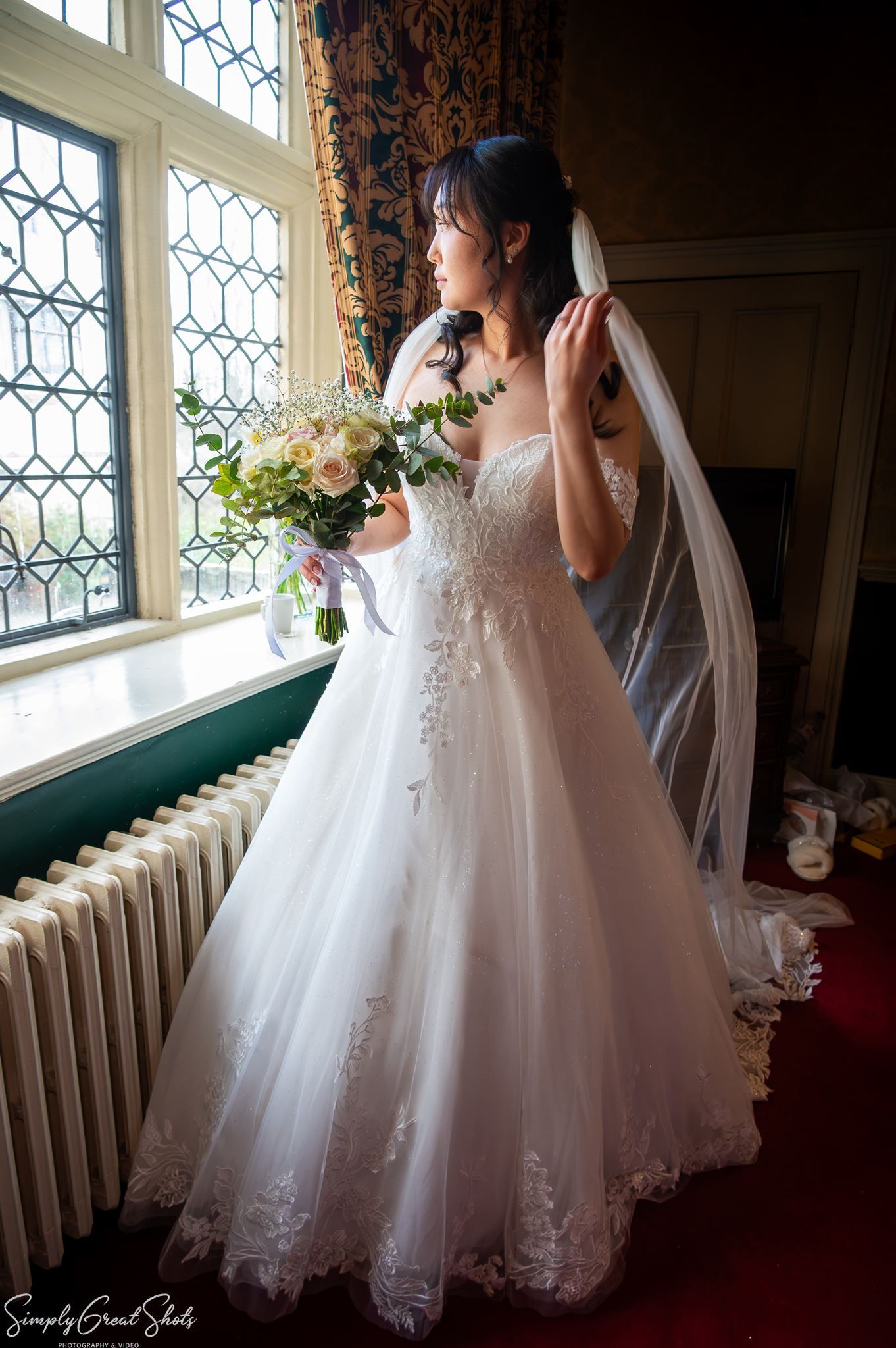 SimplyGreatShots portrait of bride Minky in her off-the-shoulder gown and veil by a window at Coombe Abbey.