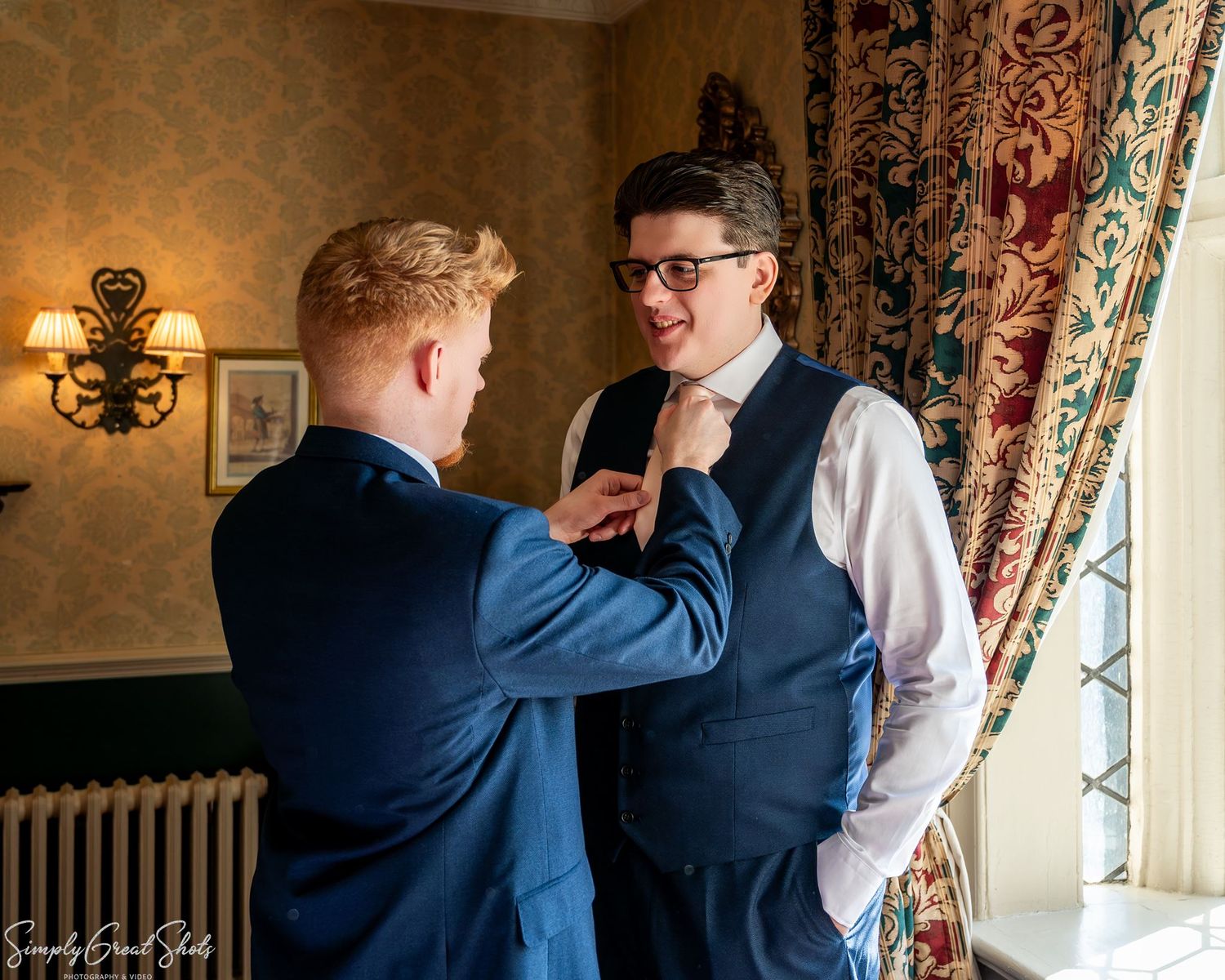 Groomsman adjusting groom Mark's tie before the wedding ceremony at Coombe Abbey Warwickshire.