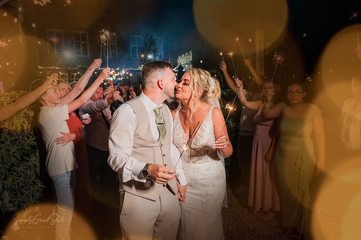 A bride and groom kiss at the end of their sparkler exit with bokeh on the outer edges of the picture.