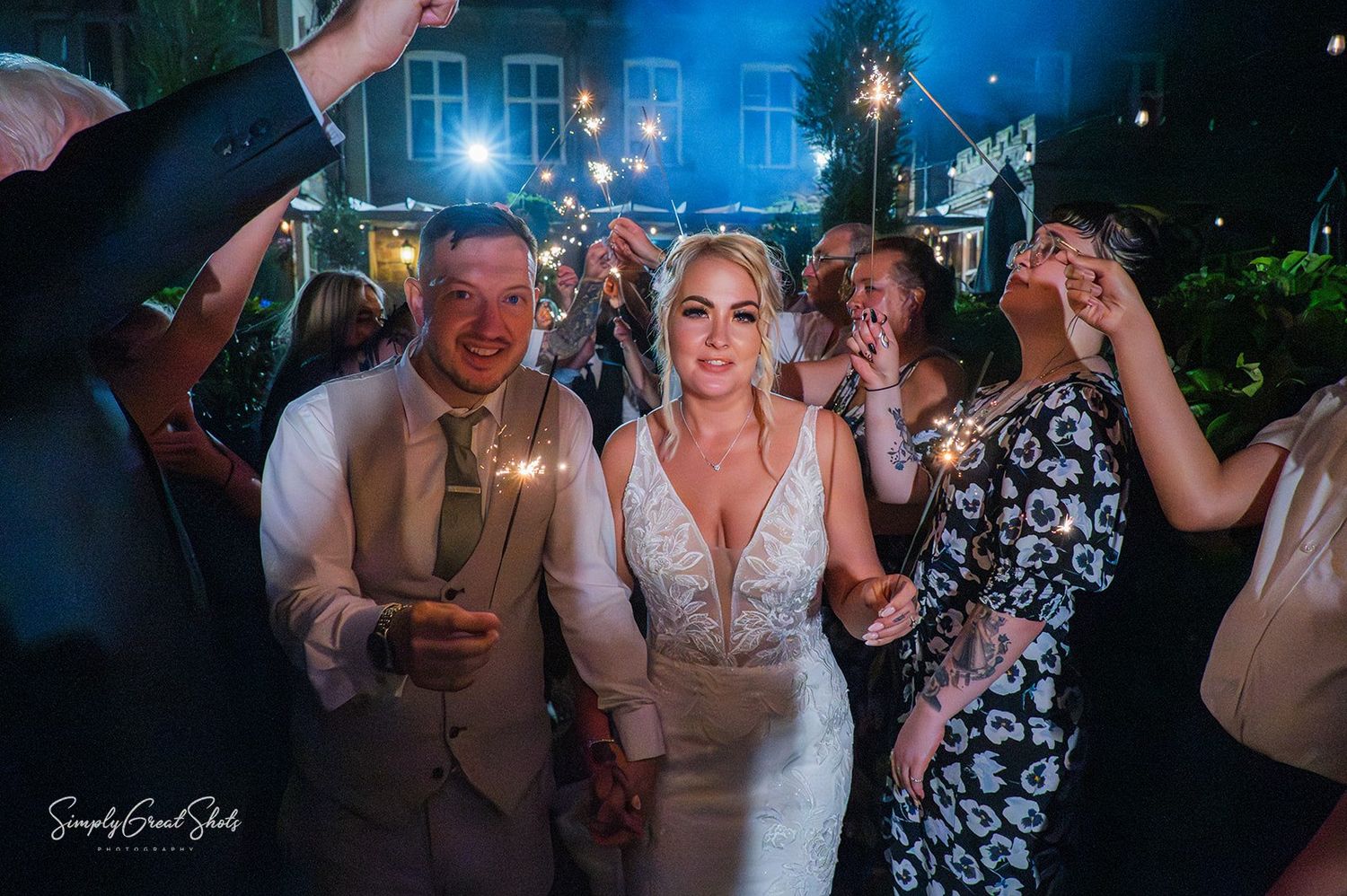 A wedding sparkler exit with people dancing and celebrating at a lively wedding reception with blue lighting and sparklers.
