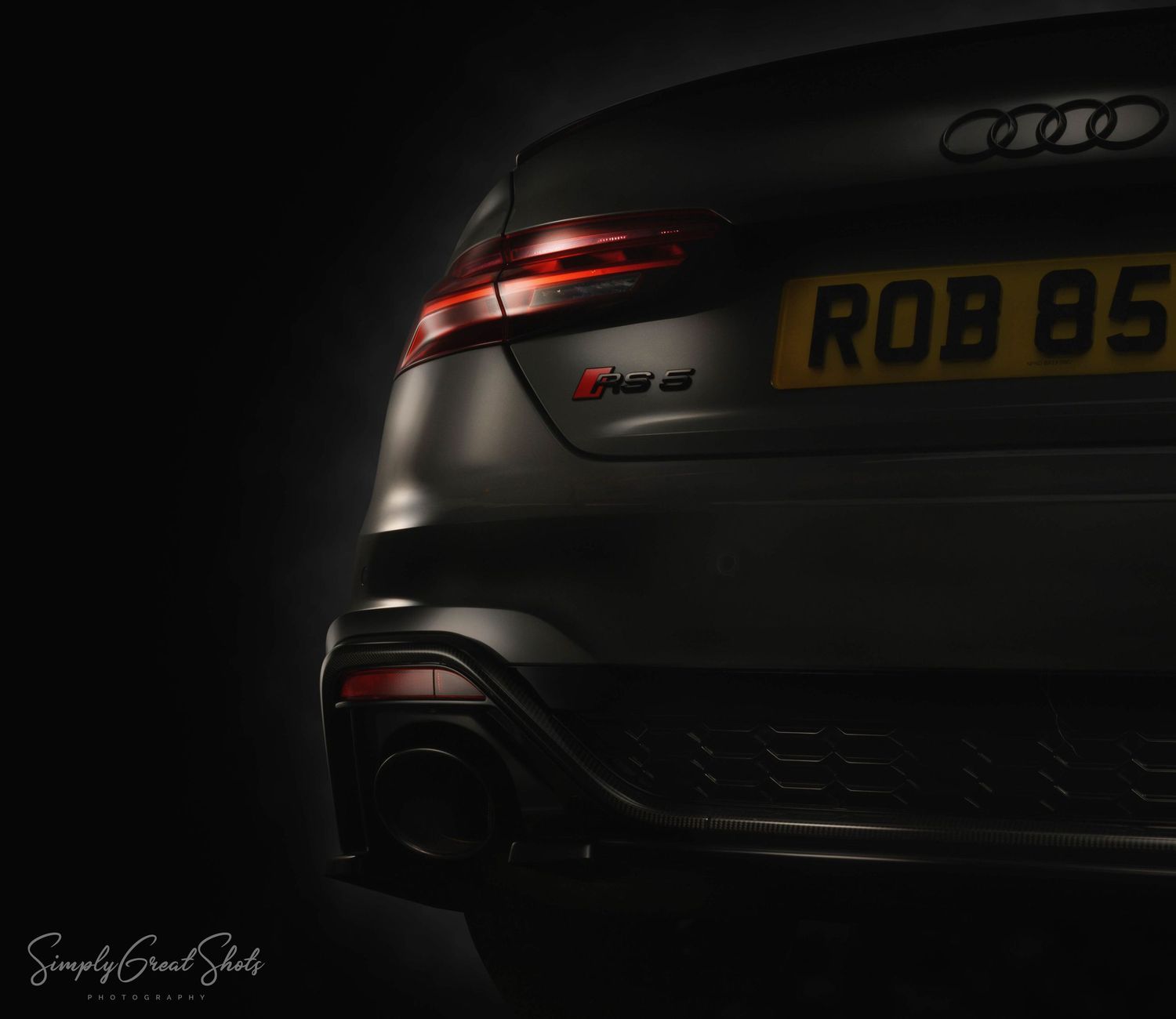 Close-up of a modern Audi RS5 rear end showing sleek taillights and license plate in dramatic dark lighting.
