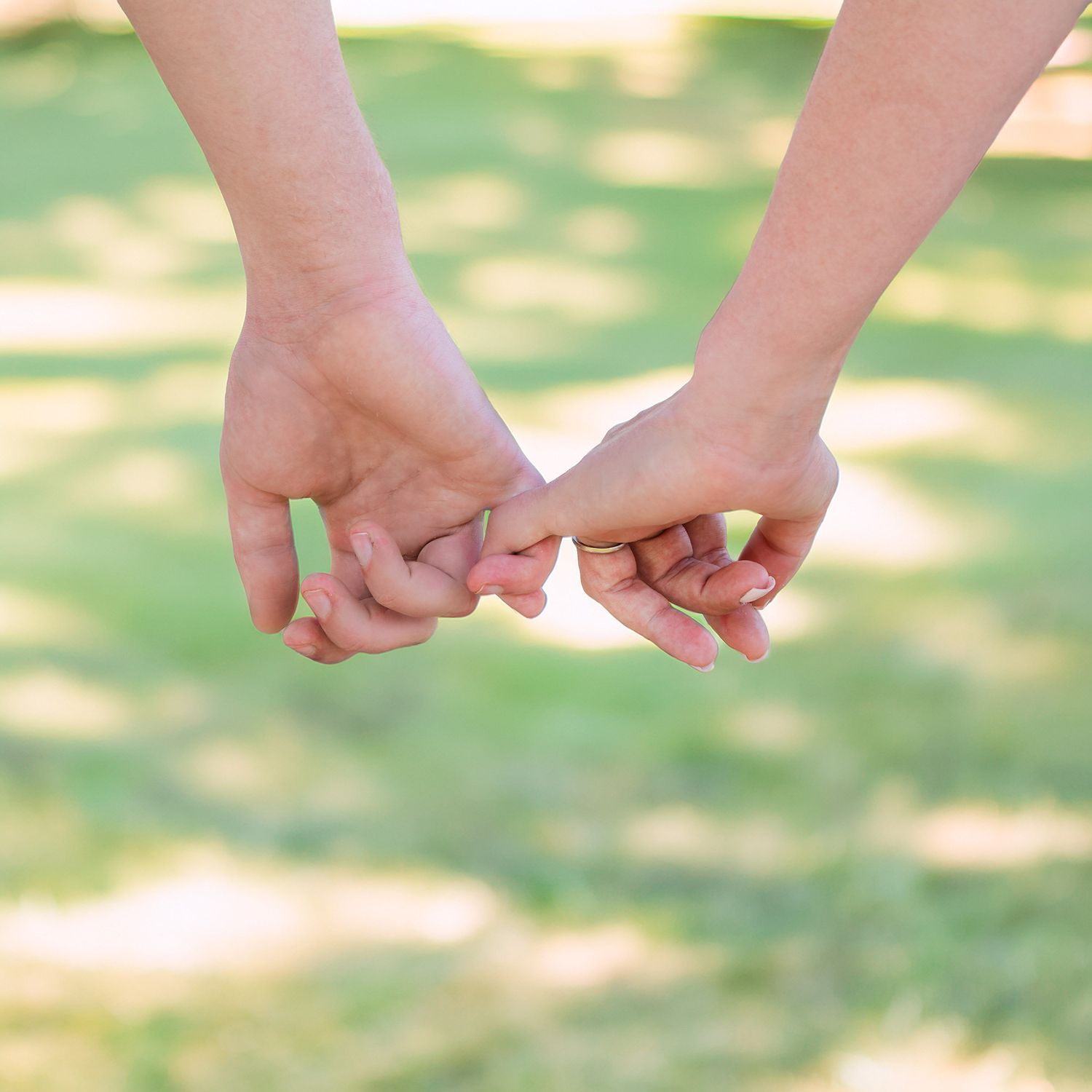 An engaged couple link their pinky fingers together whilst walking