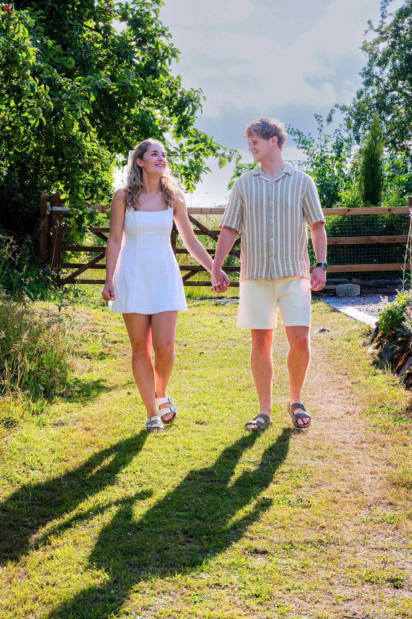 Two people walk together on a grassy path with their shadows stretching out beside them on a sunny day.