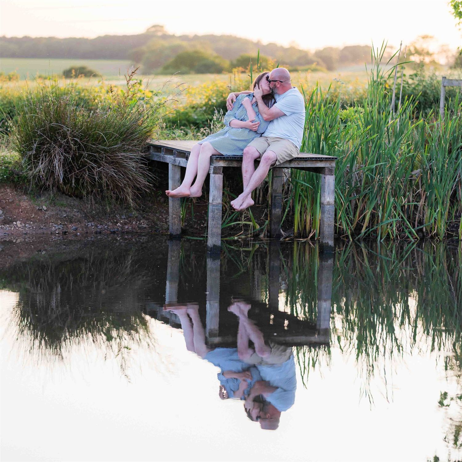 Warwickshire wedding photographer captures a kiss on a jetty with reflections of the happy couple during their pre-wedding photoshoot.