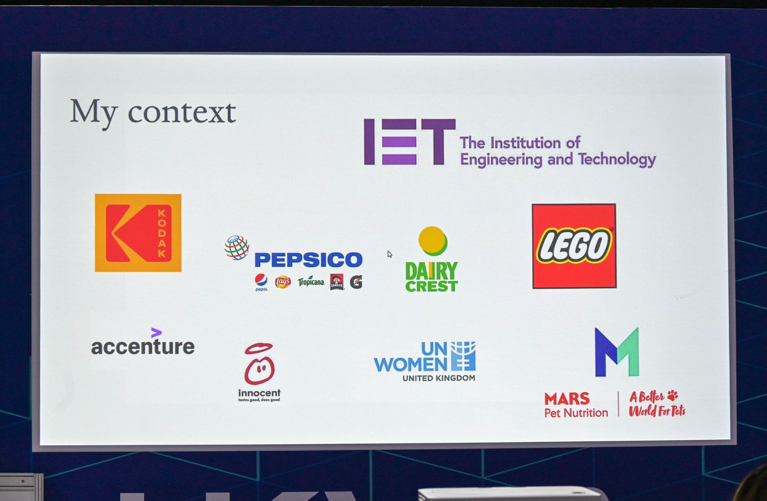 A white display screen showing corporate logos including IET, Pepsico, LEGO, and Accenture against a dark background.