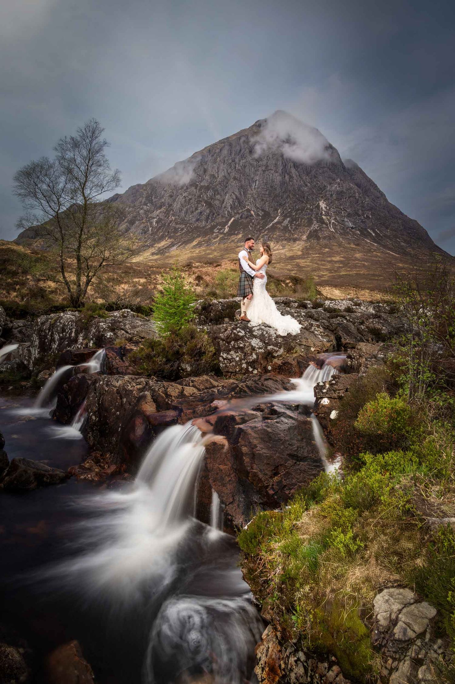 Scenic waterfall with majestic Buachaille Etive Mor mountain in Glen Etive, Scotland under moody dramatic skies.