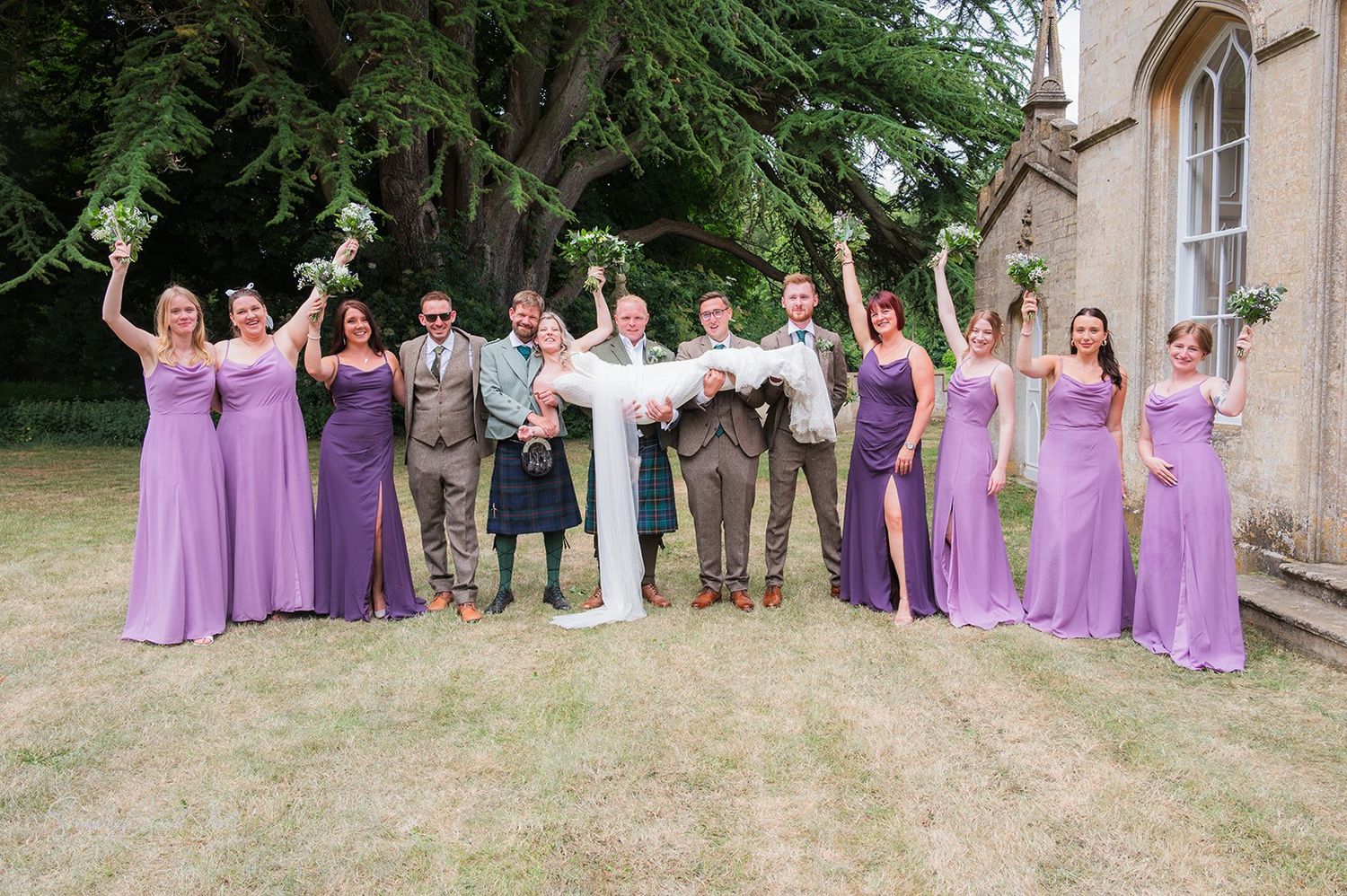 A bride is held in the air by the groom and groomsmen while the bridesmaids. cheer