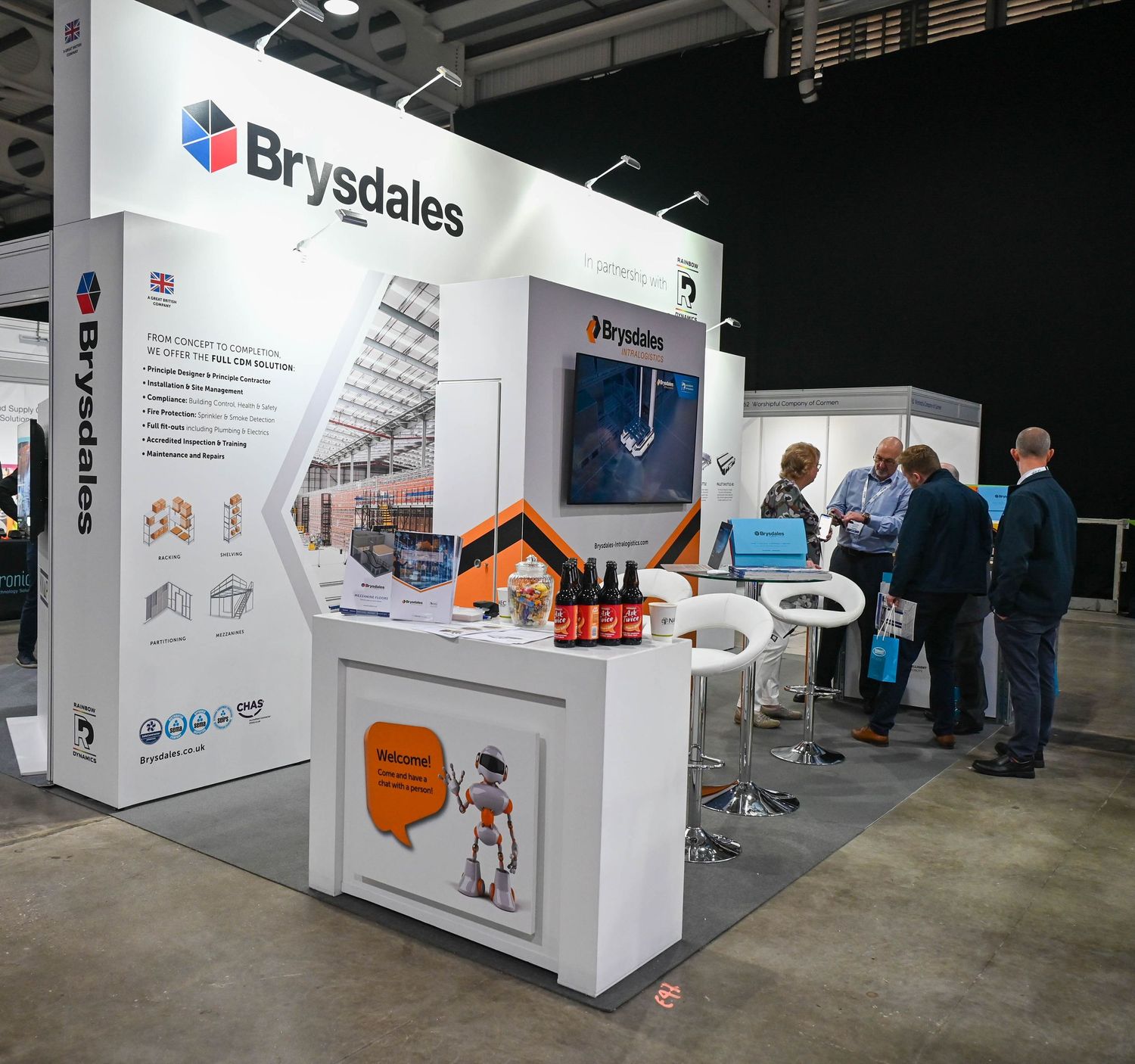Trade show booth for Brysdales company featuring white display counter with orange accents and group gathered at an exhibition.