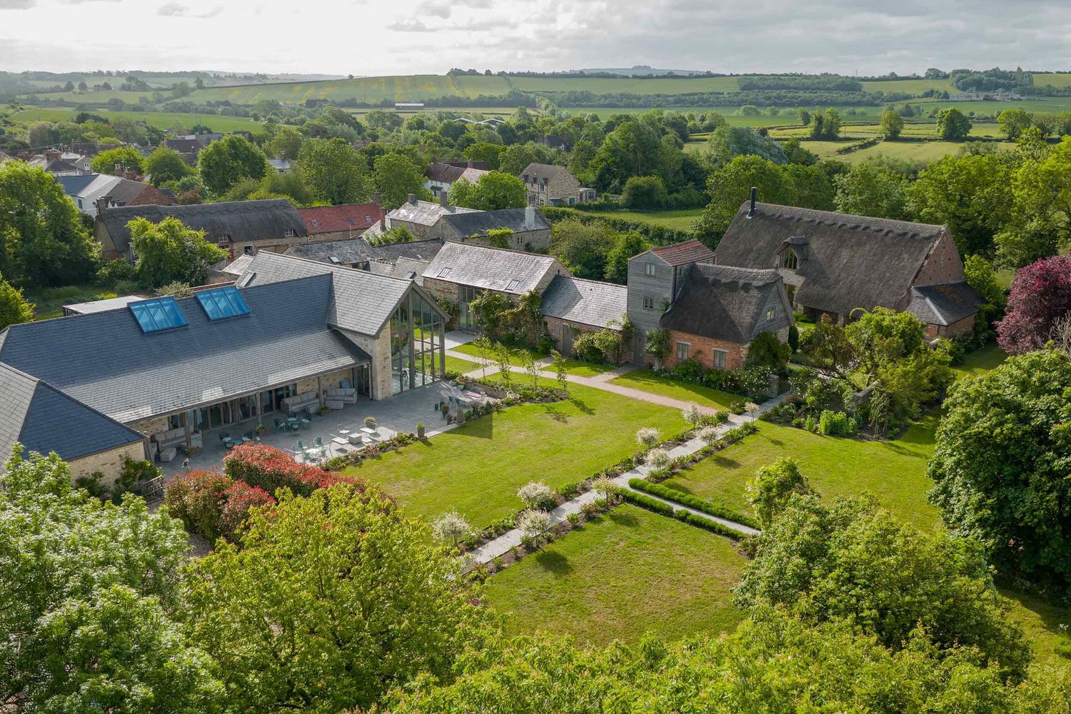 An aerial view of a rural property with modern buildings, landscaped gardens and terraced grounds surrounded by countryside.