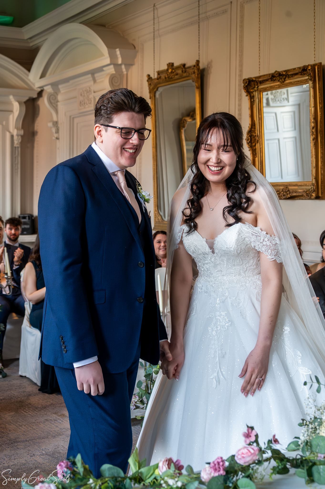 Bride Minky and groom Mark holding hands and smiling during their wedding ceremony in The Cloisters.