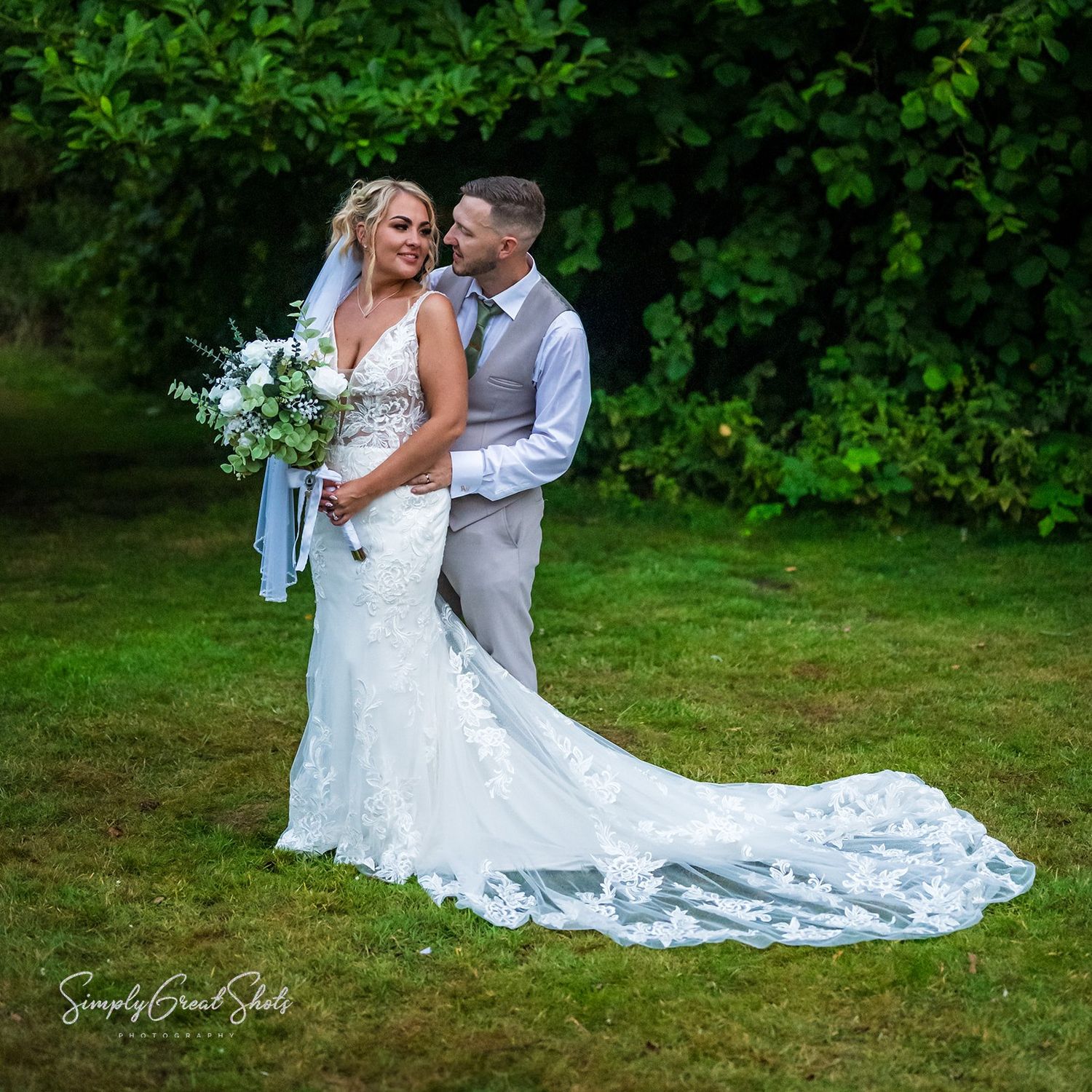 A couple celebrates their wedding day in a lush garden setting with the bride's elegant white gown trailing behind them.