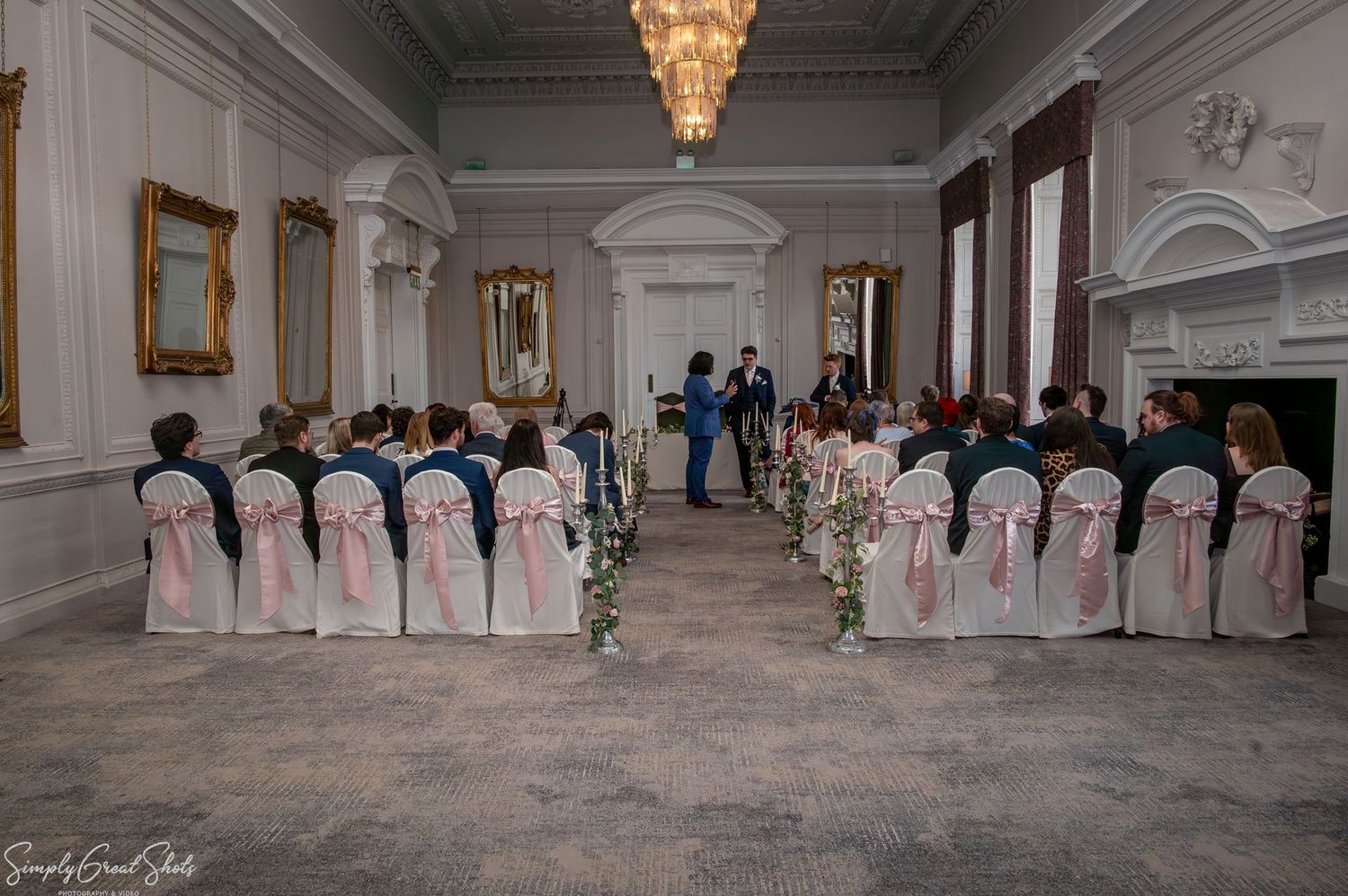 The Cloisters wedding ceremony room setup at Coombe Abbey featuring a grand chandelier and pink bows.
