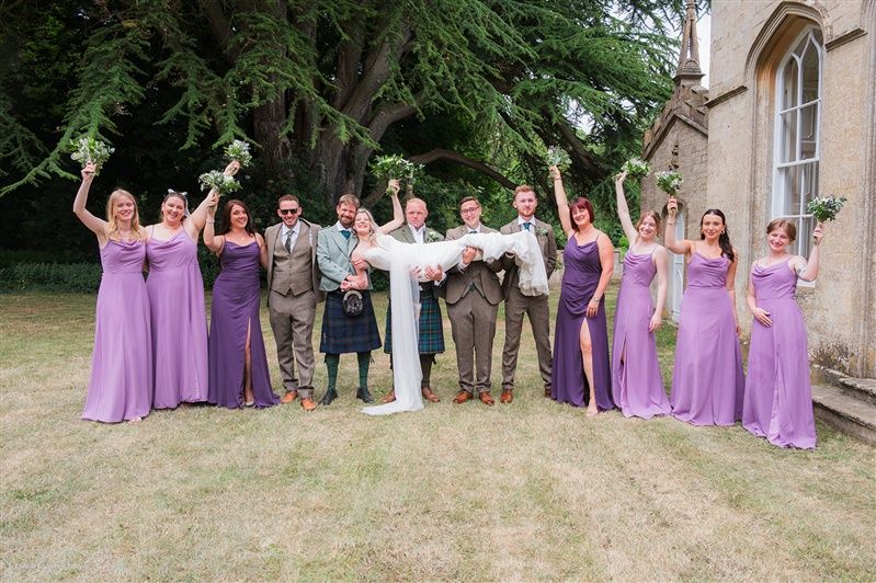 Wedding party in lilac gowns & kilts cheering as bride is lifted aloft outside Fort Henry, Rutland – SimplyGreatShots Photography