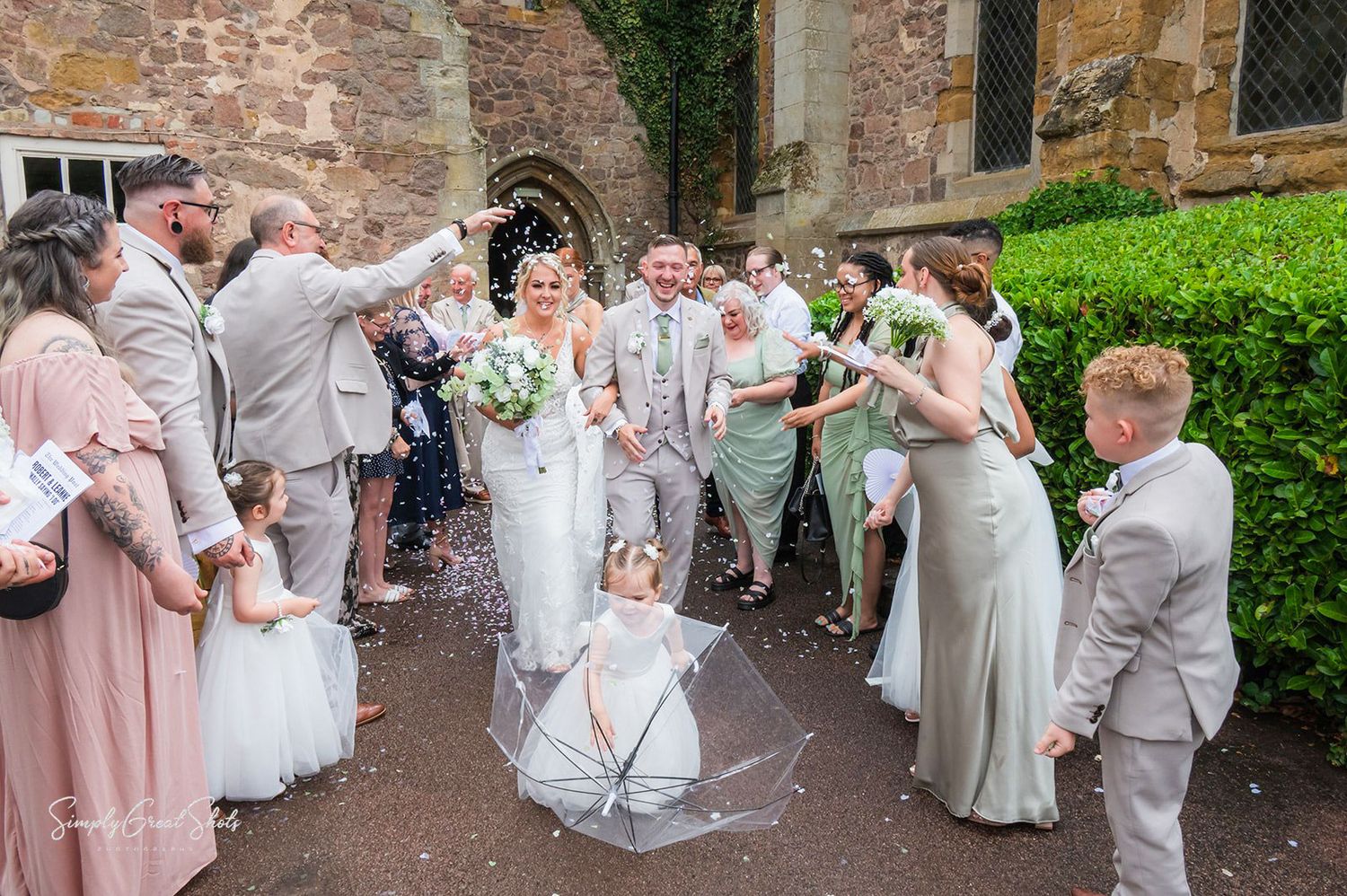 Wedding party poses outside Rothley Court in Leicestershire in light pink and gray formal attire with bouquets as confetti is thrown.