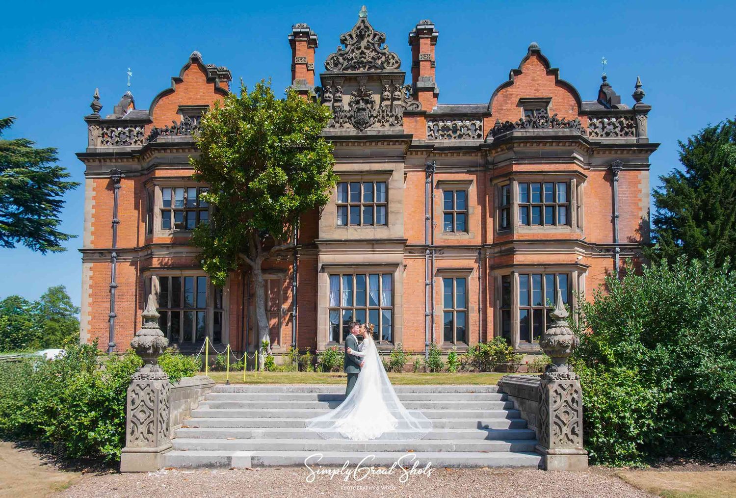 Bride and groom standing on the steps in the back garden of Beaumanor Hall, Leicestershire.