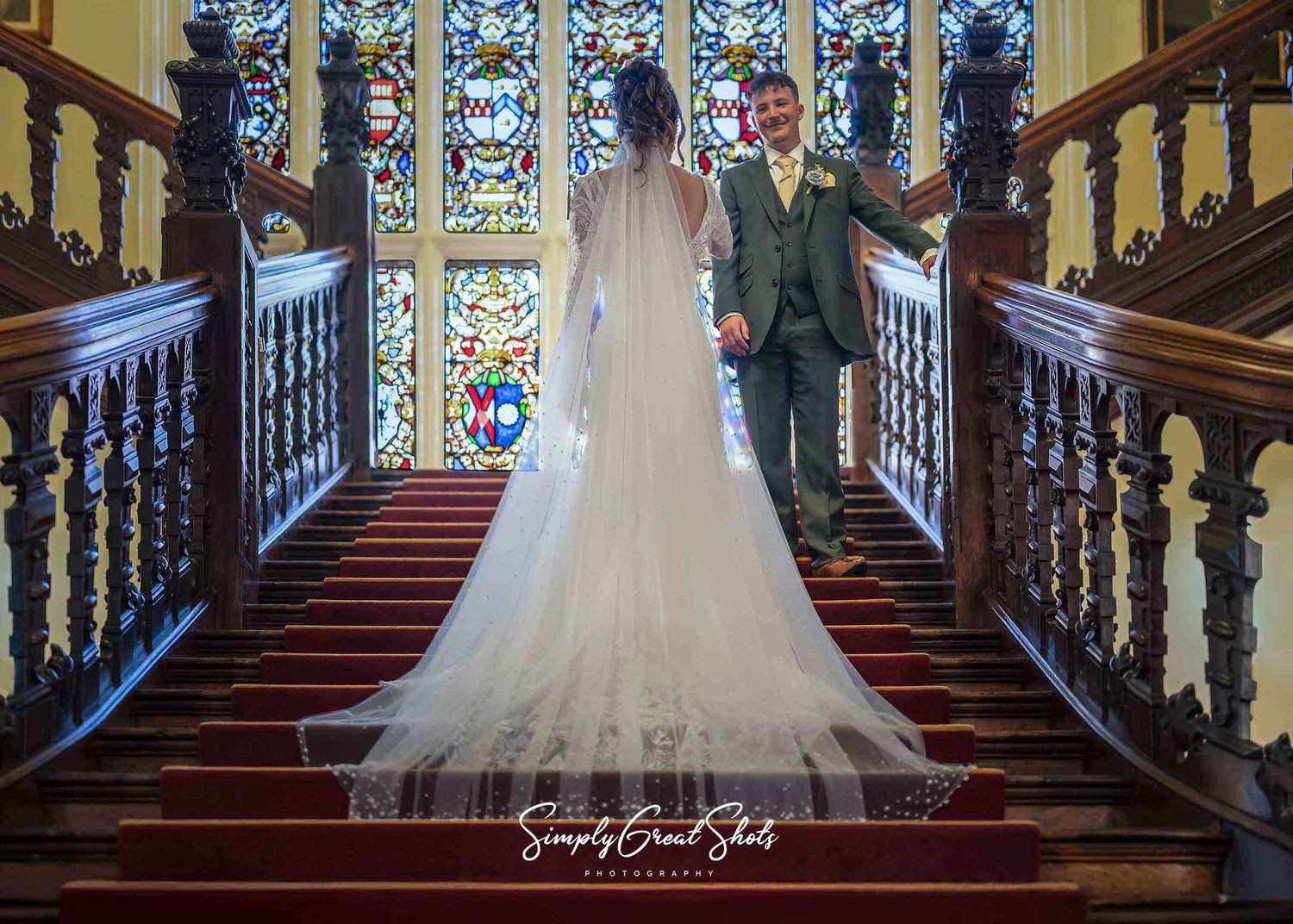 Beaumanor Hall wedding photographer captures the bride and groom on the grand staircase with string glass windows in the background
