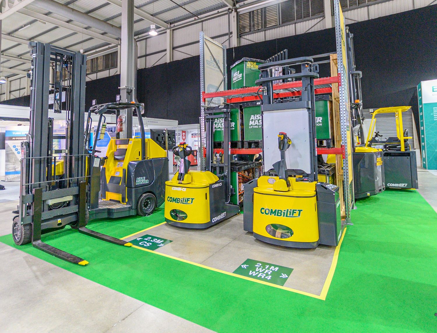 Colorful fleet of industrial forklifts displayed on green flooring at a warehouse or equipment showroom.
