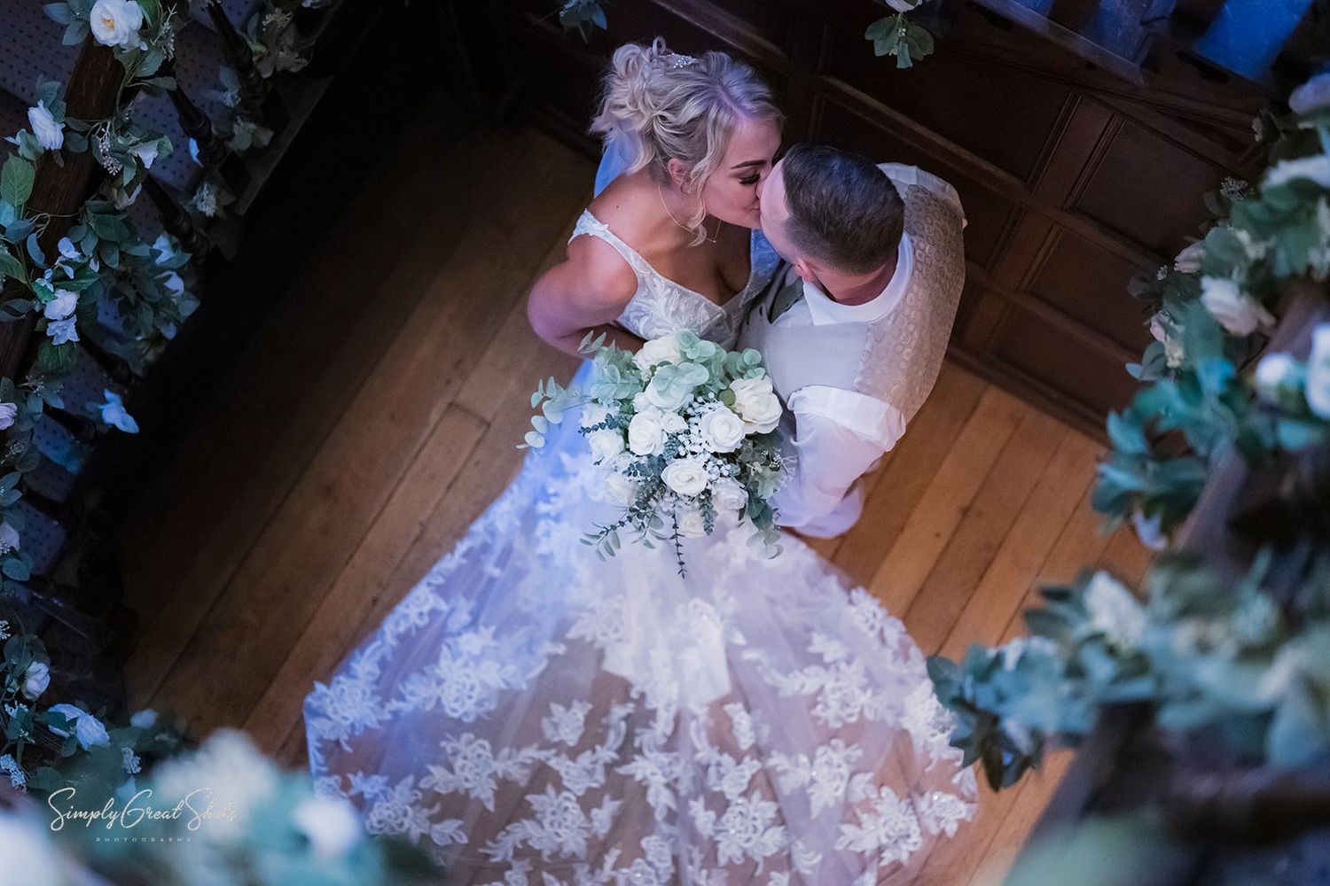 A close-up view of a white wedding dress with lace details and tulle fabric laying on a hardwood floor.