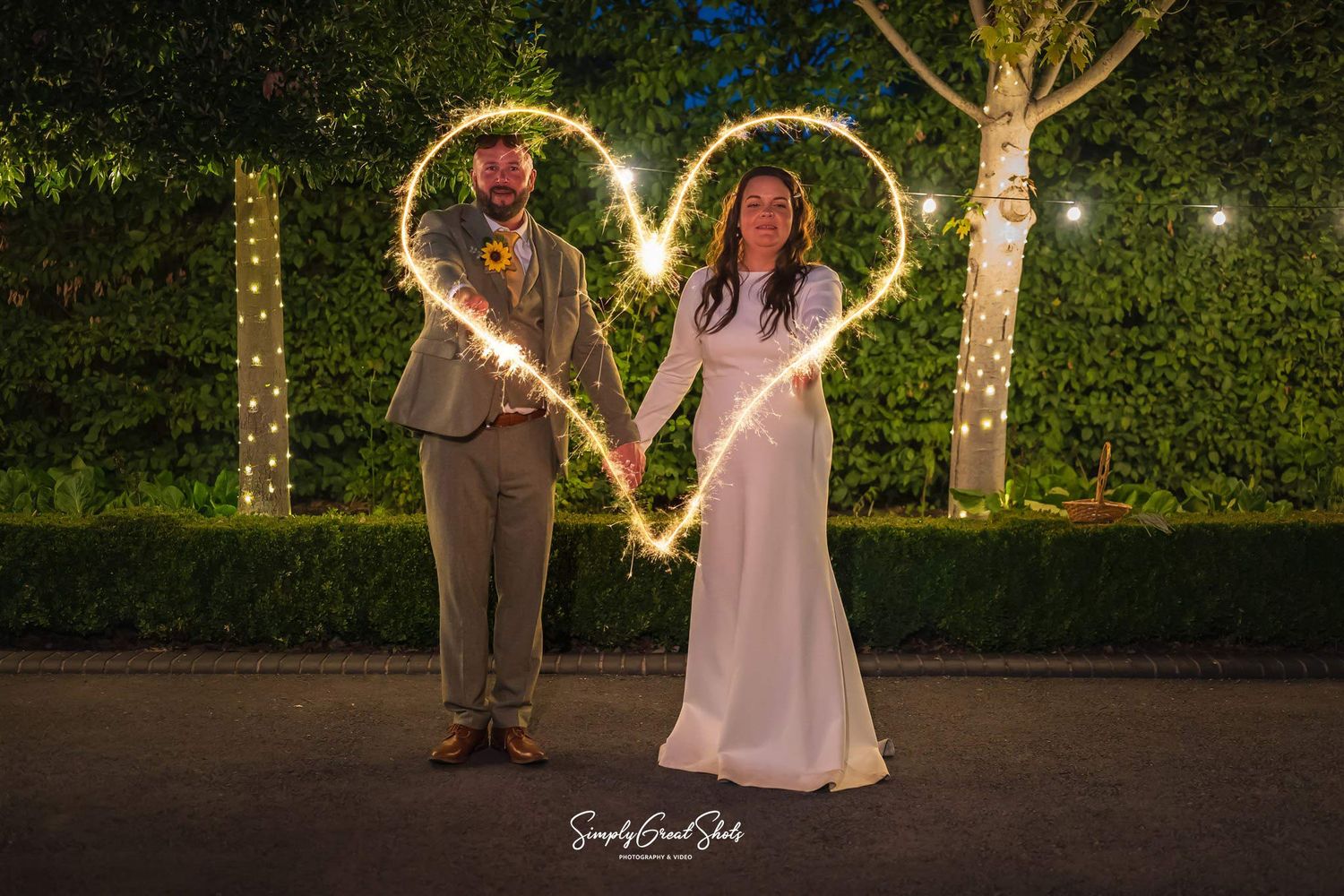 A bride and groom making a heart shape with sparklers into the evening on their wedding day.