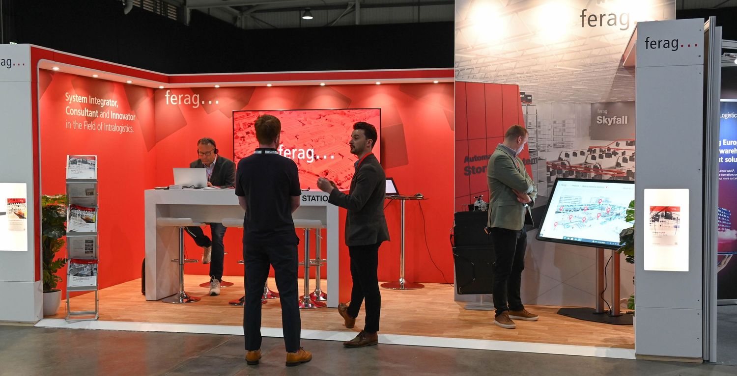 A modern trade show booth display with vibrant red walls and people interacting with digital kiosks.
