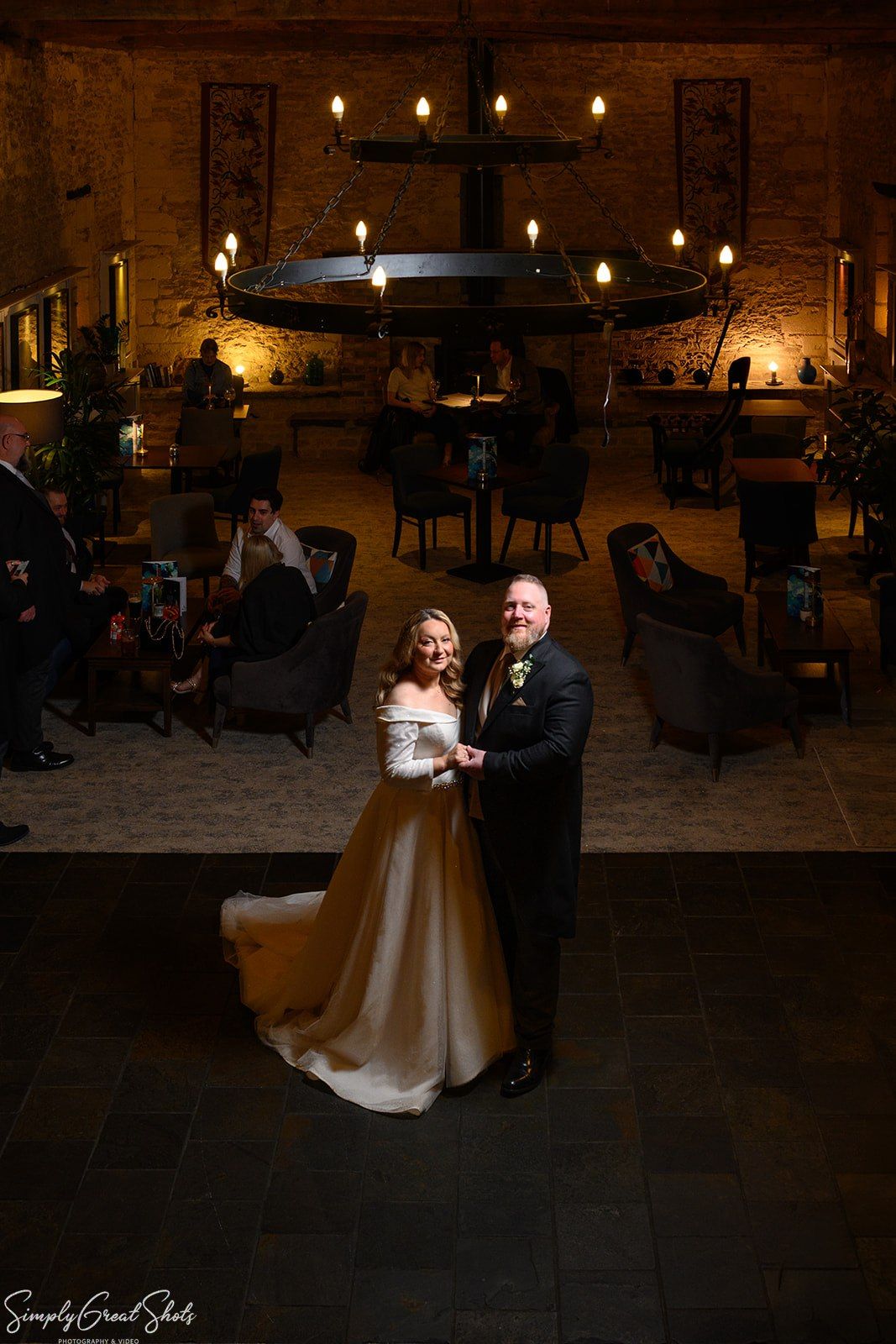 Bride and groom standing in elegant candlelit reception hall with dramatic iron chandelier at voco Oxford Thames wedding venue