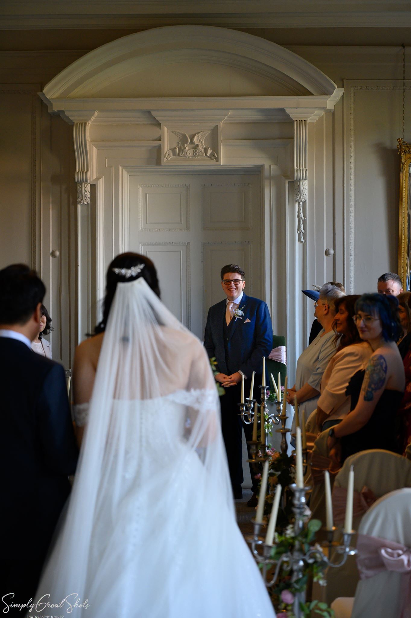 Groom Mark looks back towards Bride Minky in the altar of The Cloisters at Coombe Abbey.