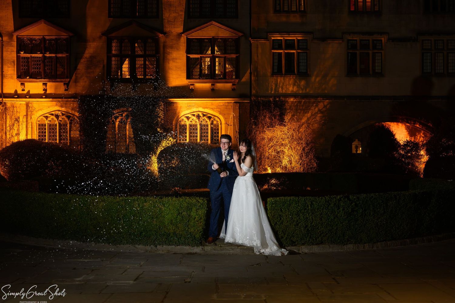 SimplyGreatShots capturing bride Minky and groom Mark spraying champagne at night in front of Coombe Abbey.