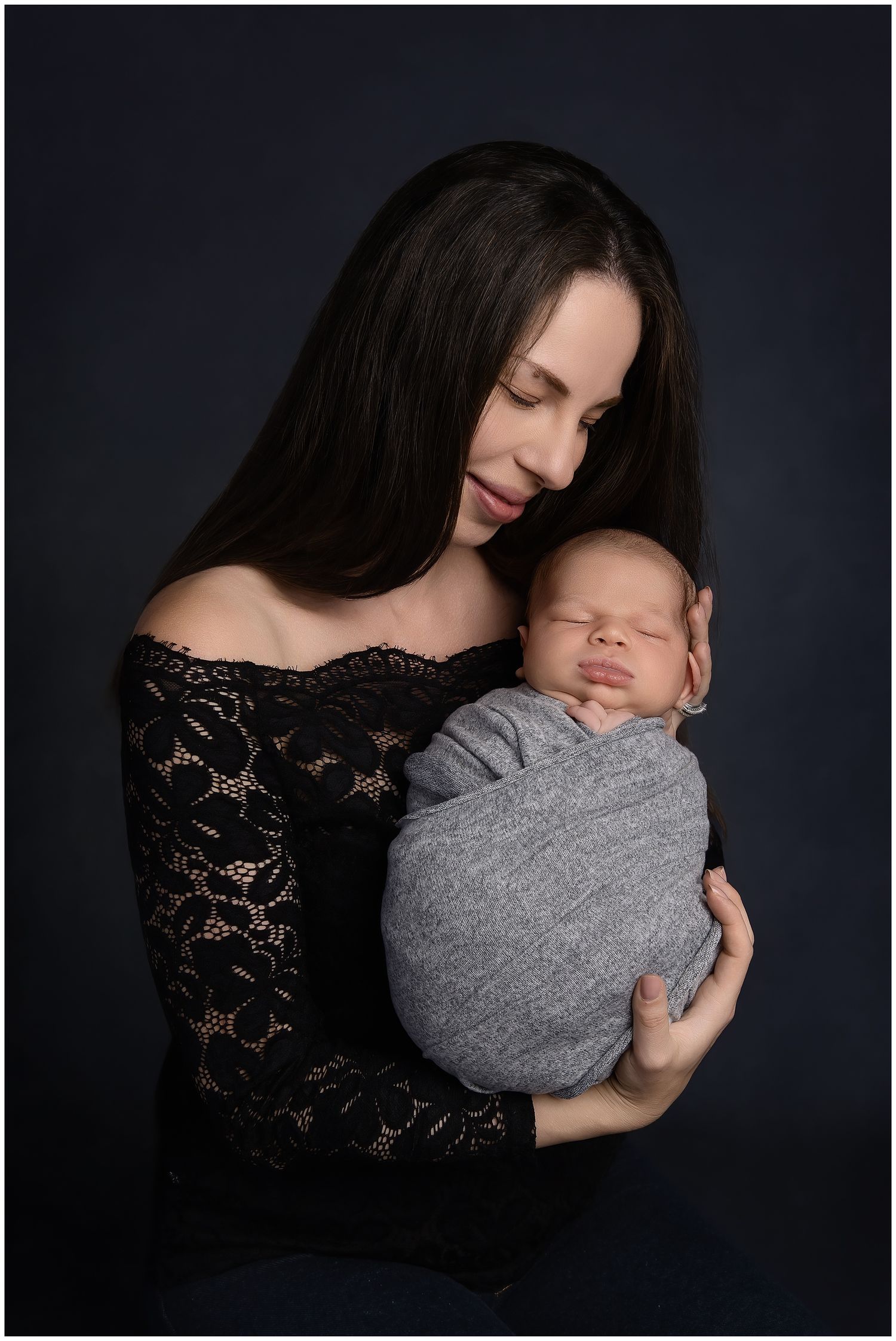Newborn portrait with mother cradling swaddled baby boy.