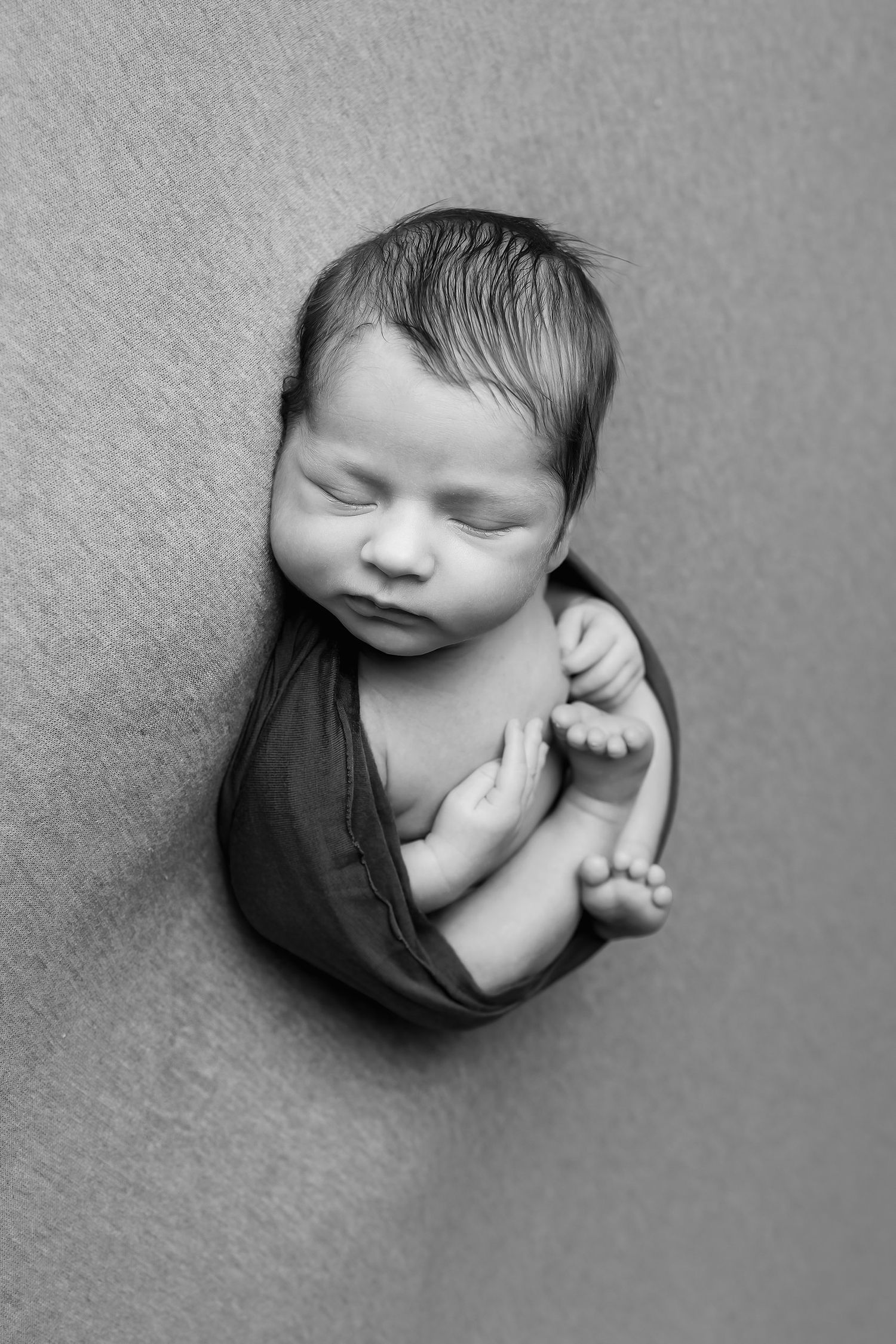 Black and white newborn photography in Austin featuring baby wrapped and posed on neutral textured backdrop