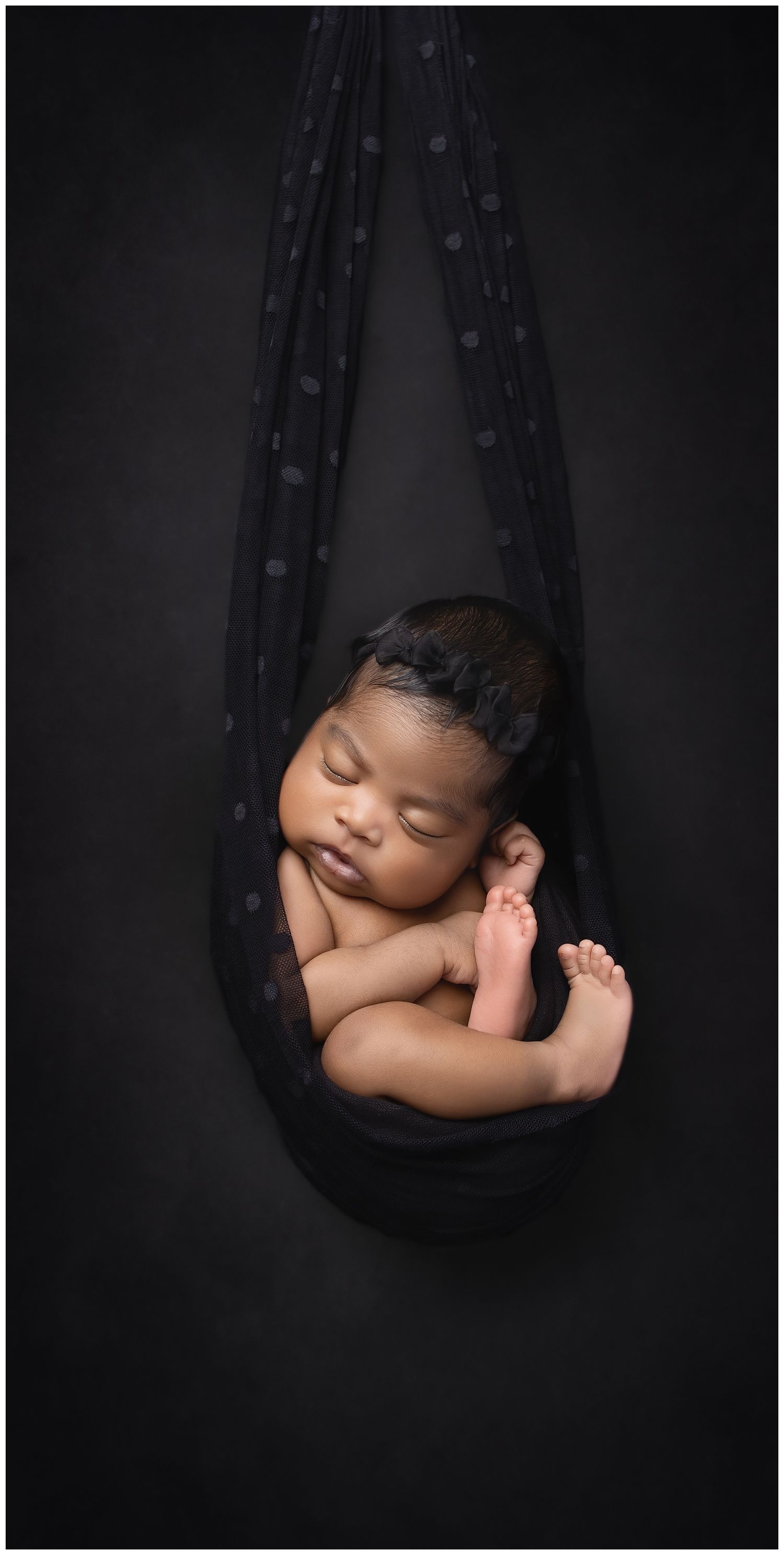 Fine art newborn photography in Austin featuring baby posed in black fabric sling on dark backdrop