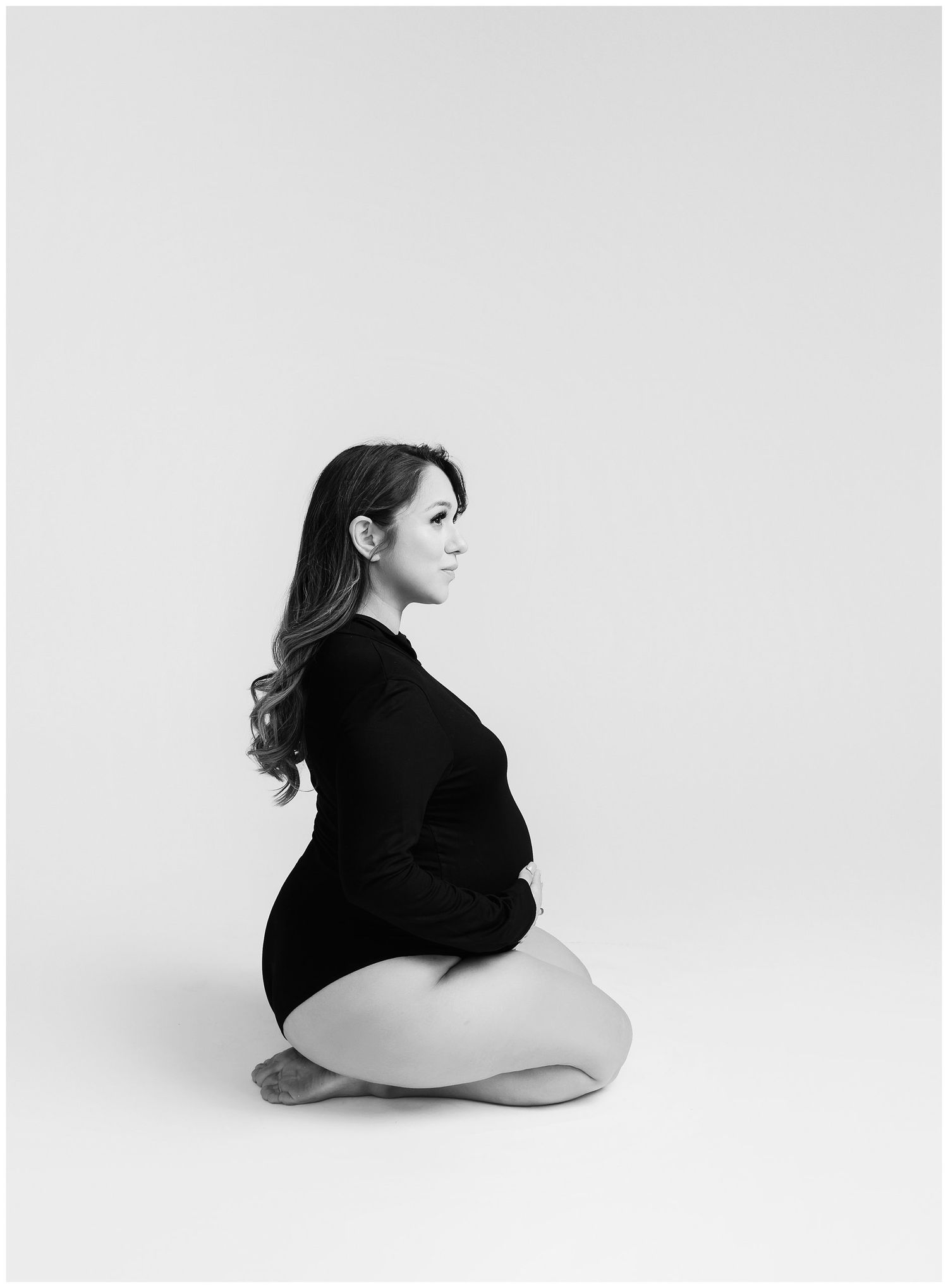 Modern black and white maternity photo of mom kneeling in black bodysuit at Austin Maternity Studio.