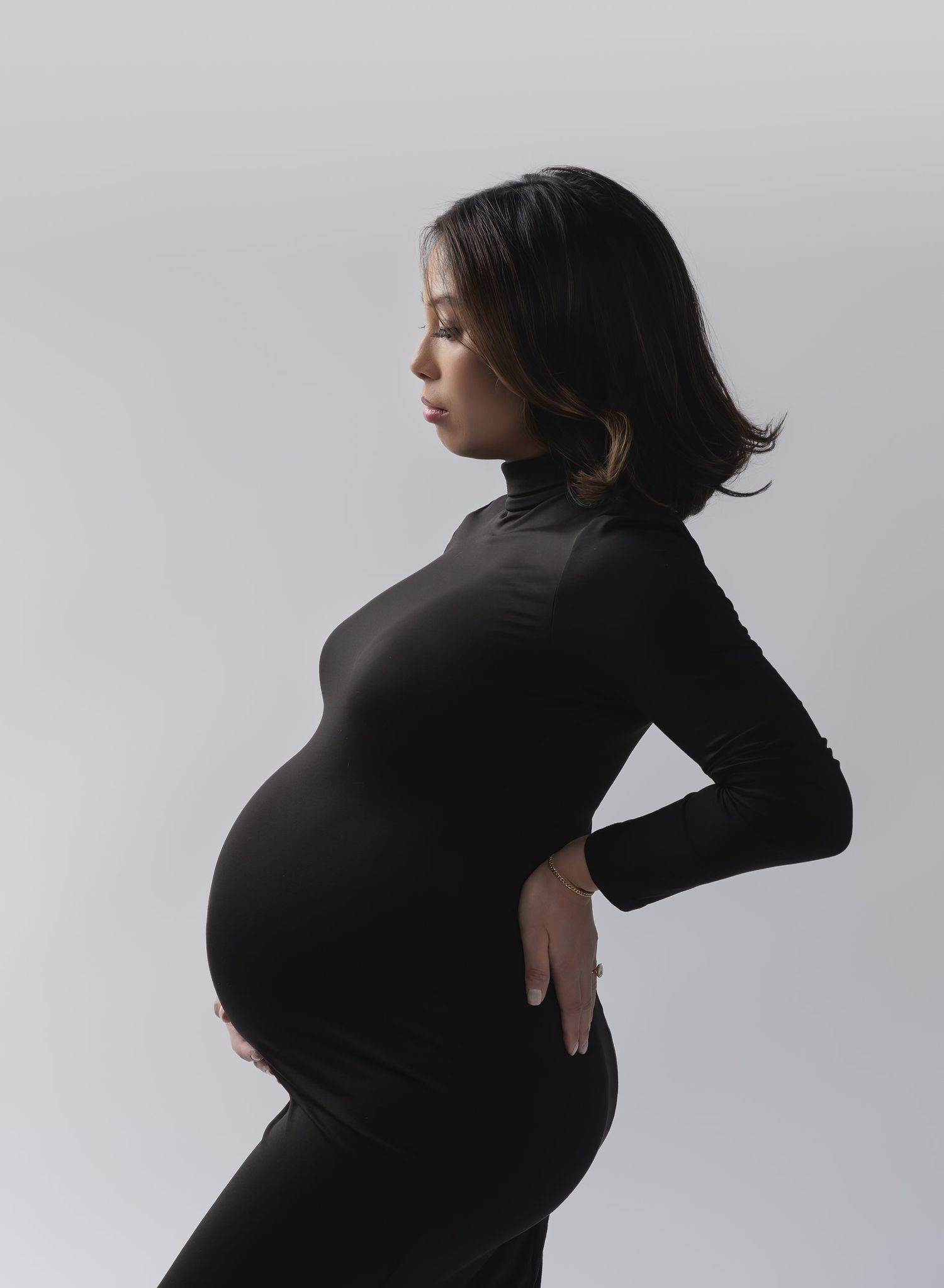 Valerie Kay Photography Modern Maternity portrait of beautiful mom in black bodycon dress in profile to the camera on white background.