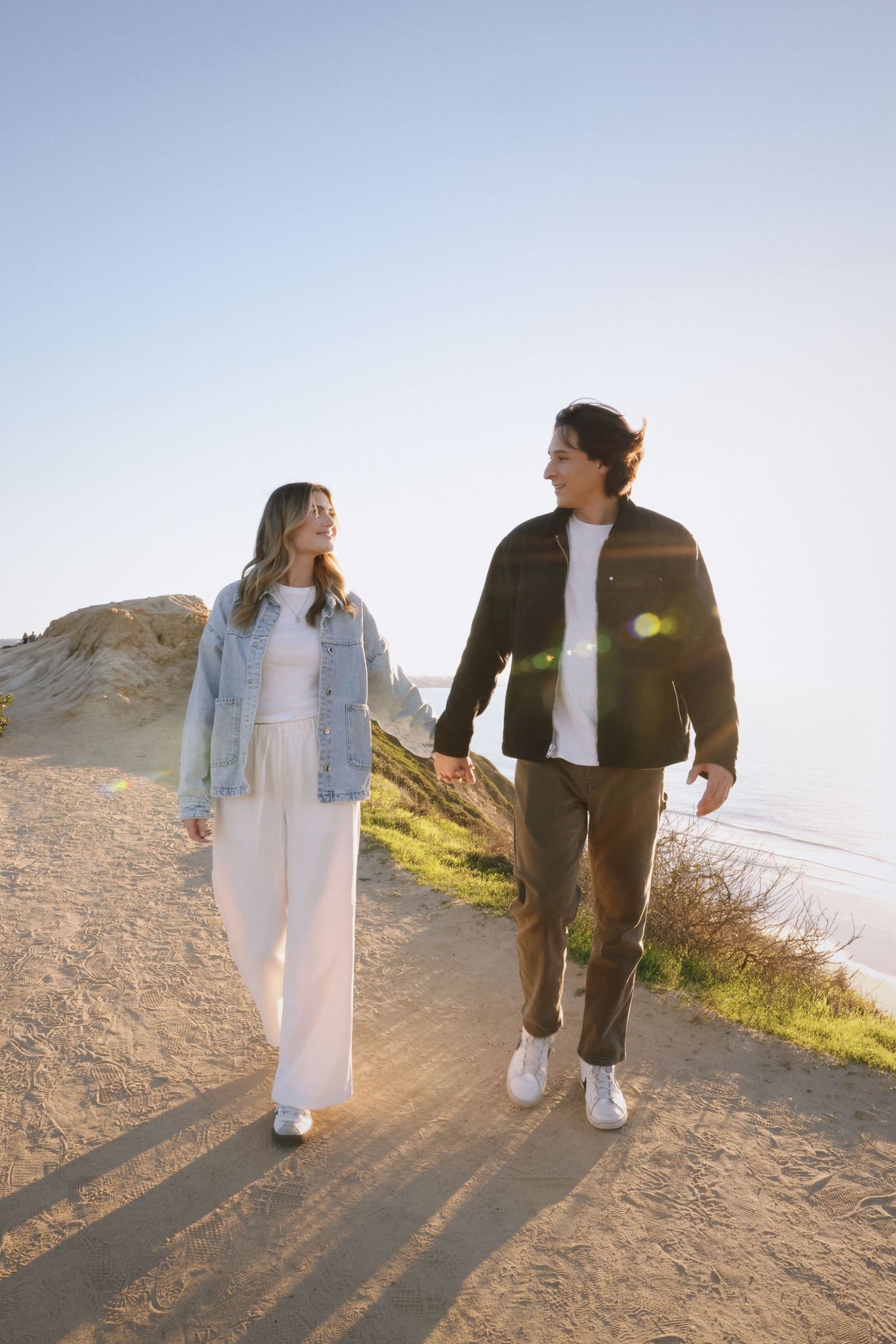 couple holding hands walking towards viewer at the torrey pines gliderport with the ocean in the background