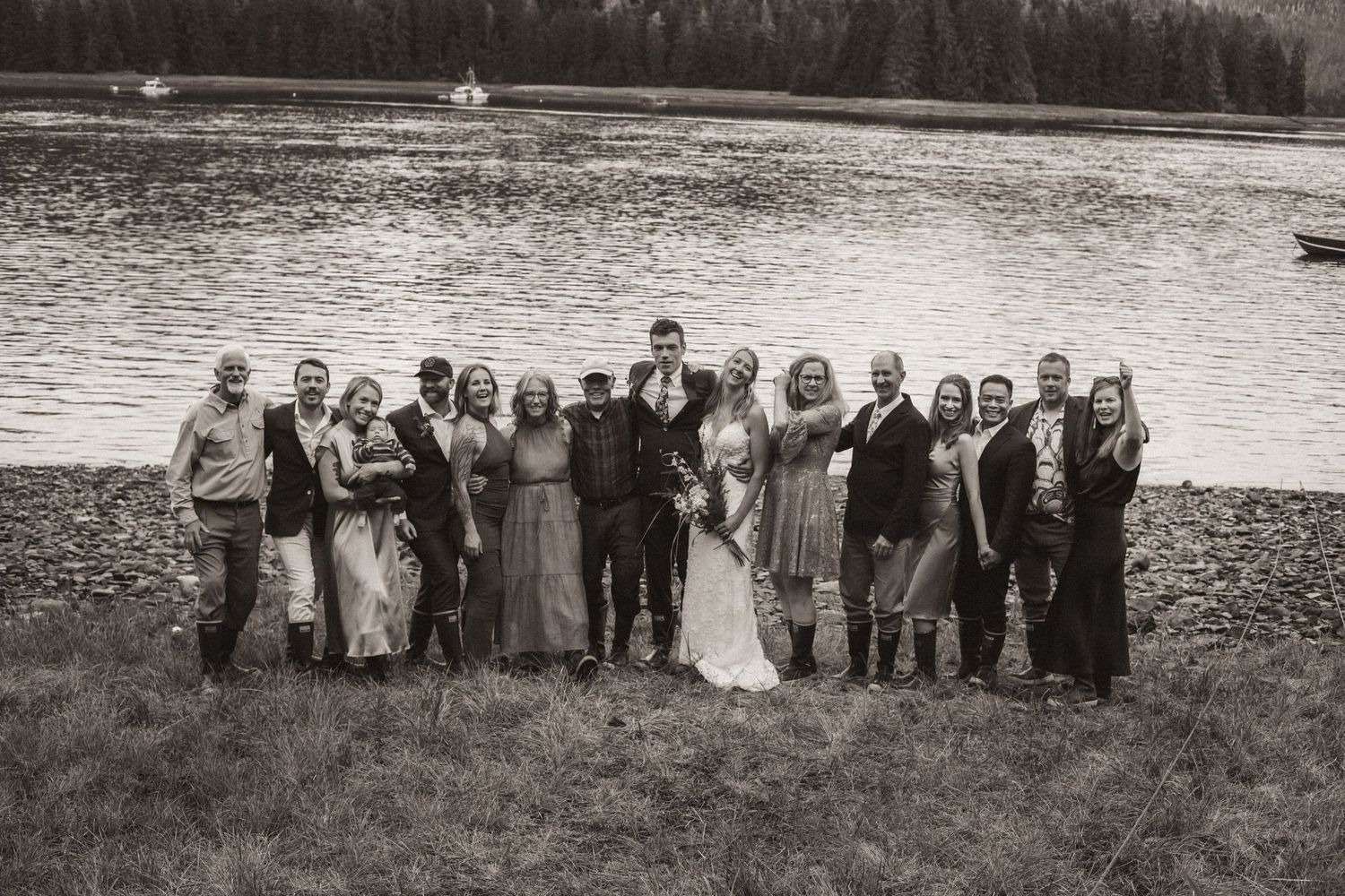 Wedding party poses together on shoreline with mountain lake backdrop in monochrome in Alaska.