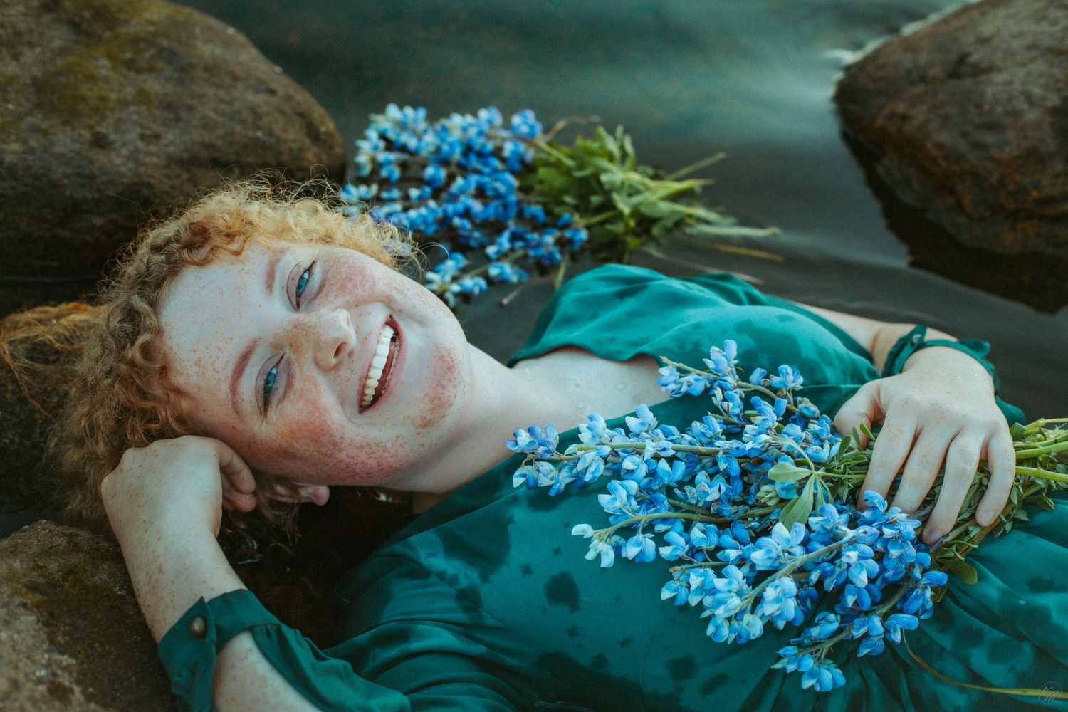 Joyful expression in a teal dress with blue flowers against water backdrop.