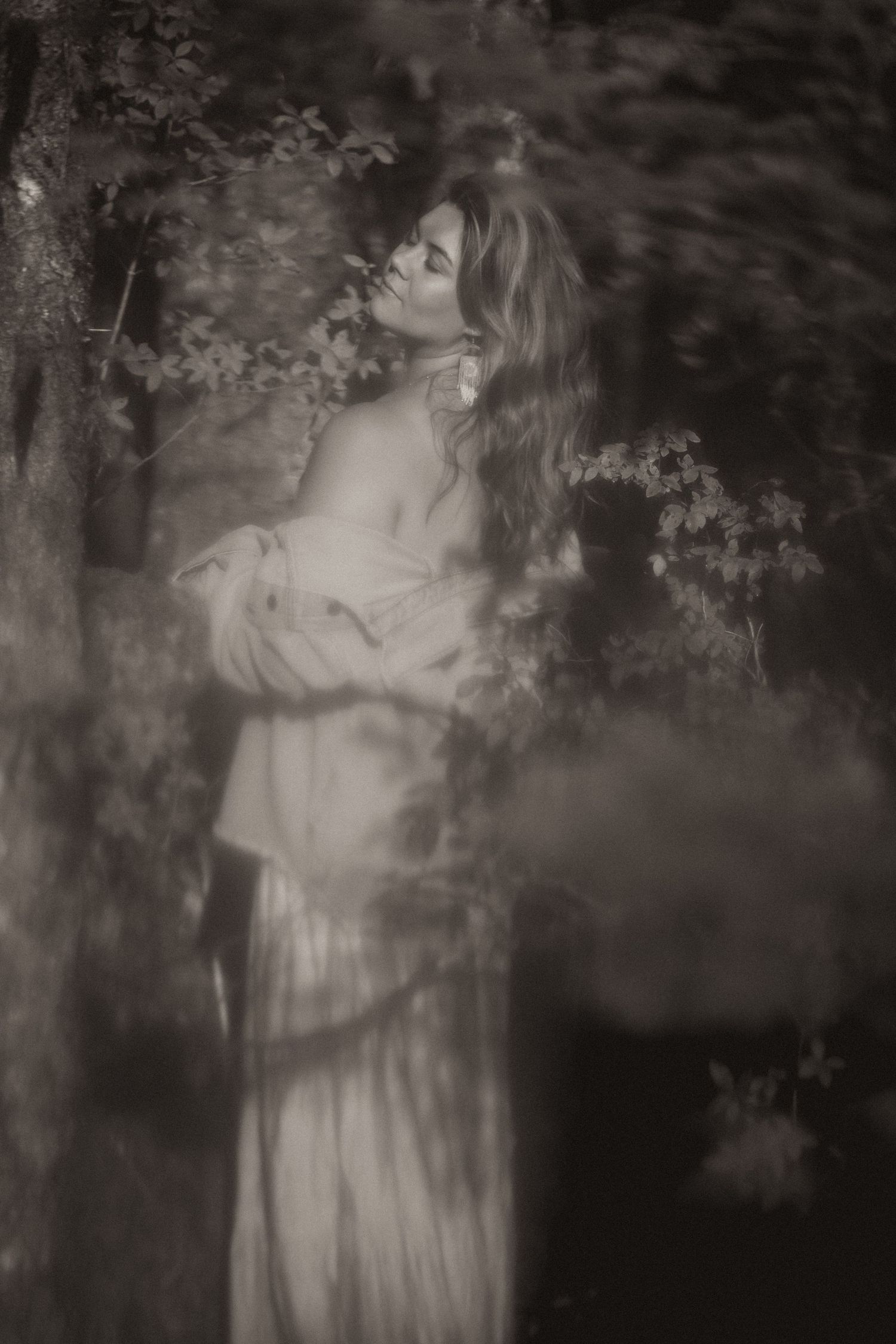 Ethereal black and white portrait of a woman in a flowing dress among misty forest trees.