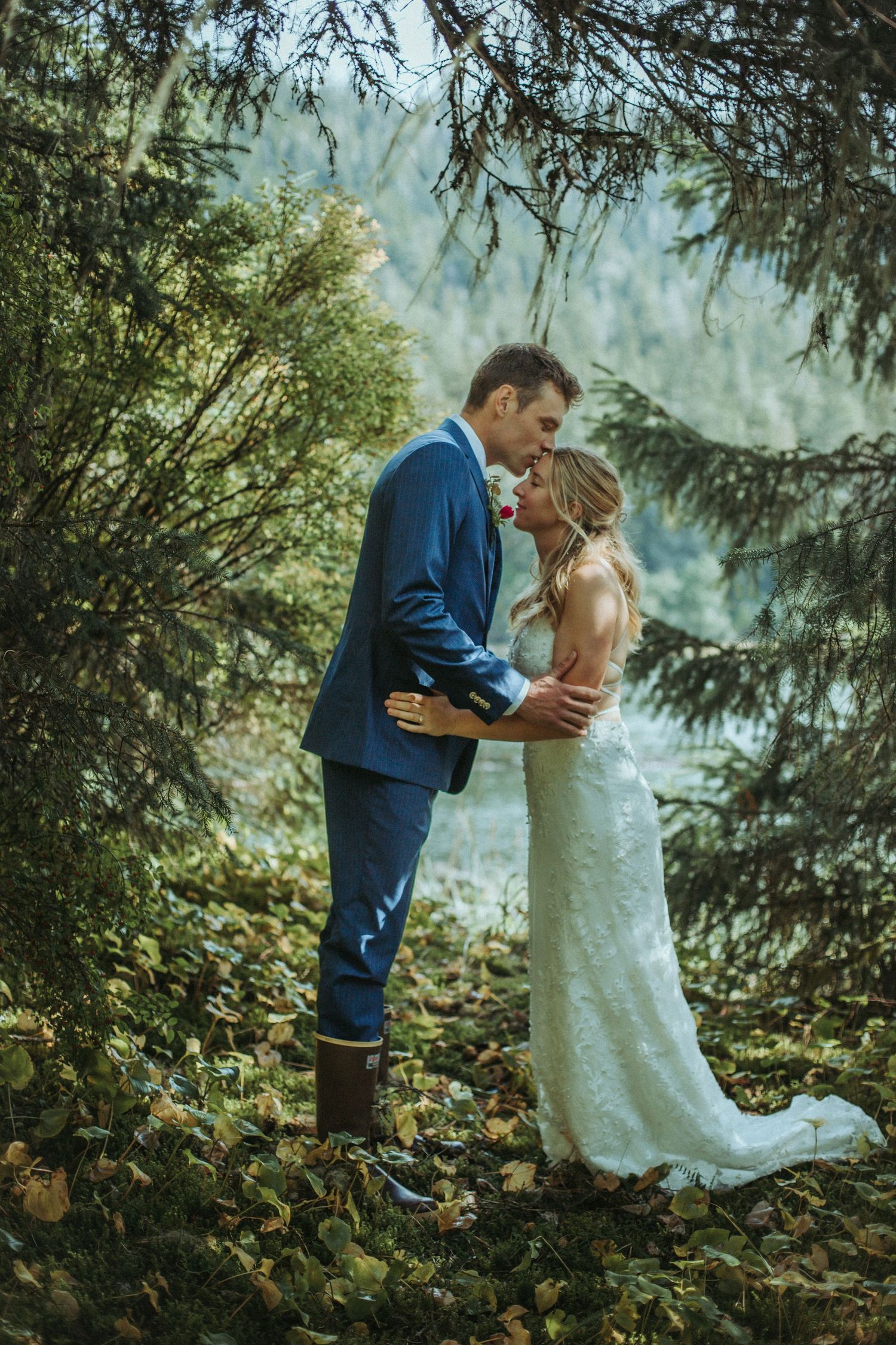 A romantic wedding photo of a couple sharing an intimate moment in a lush forest setting in Alaska.